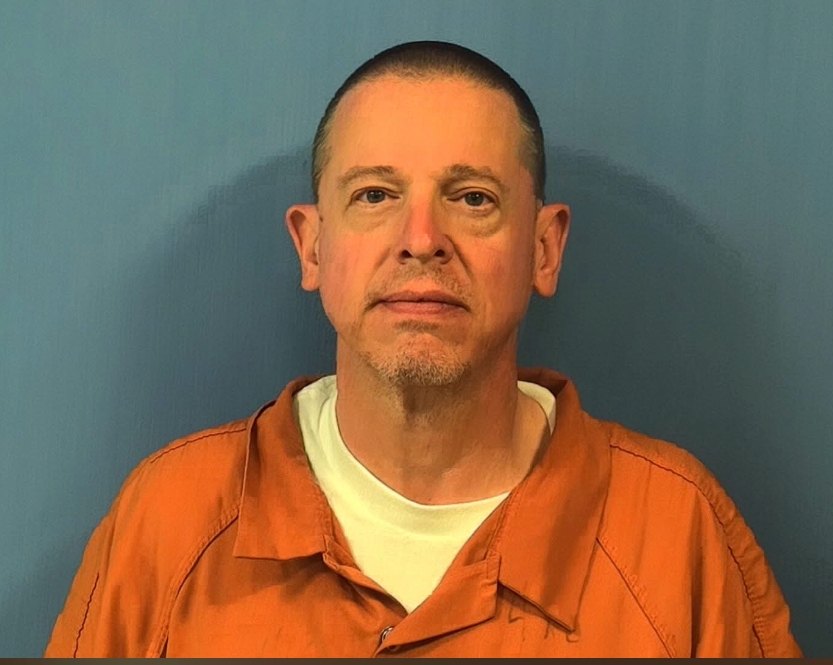 Booking photo of a man with a shaved head and goatee wearing an orange jail jumpsuit.