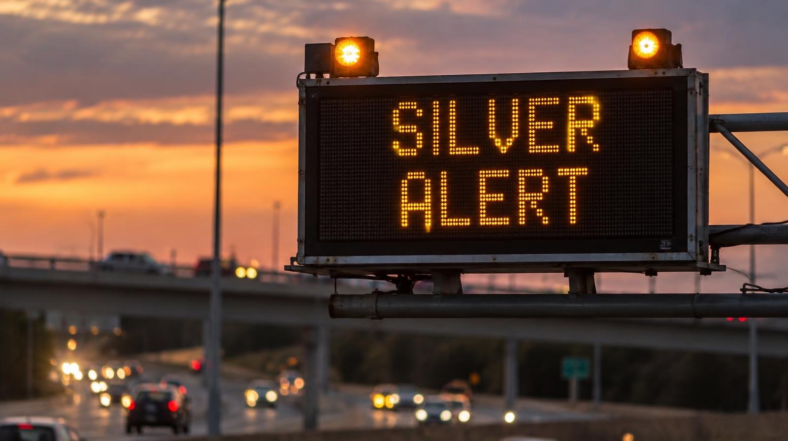 Electronic highway sign displaying a Silver Alert with amber flashing lights at dusk.