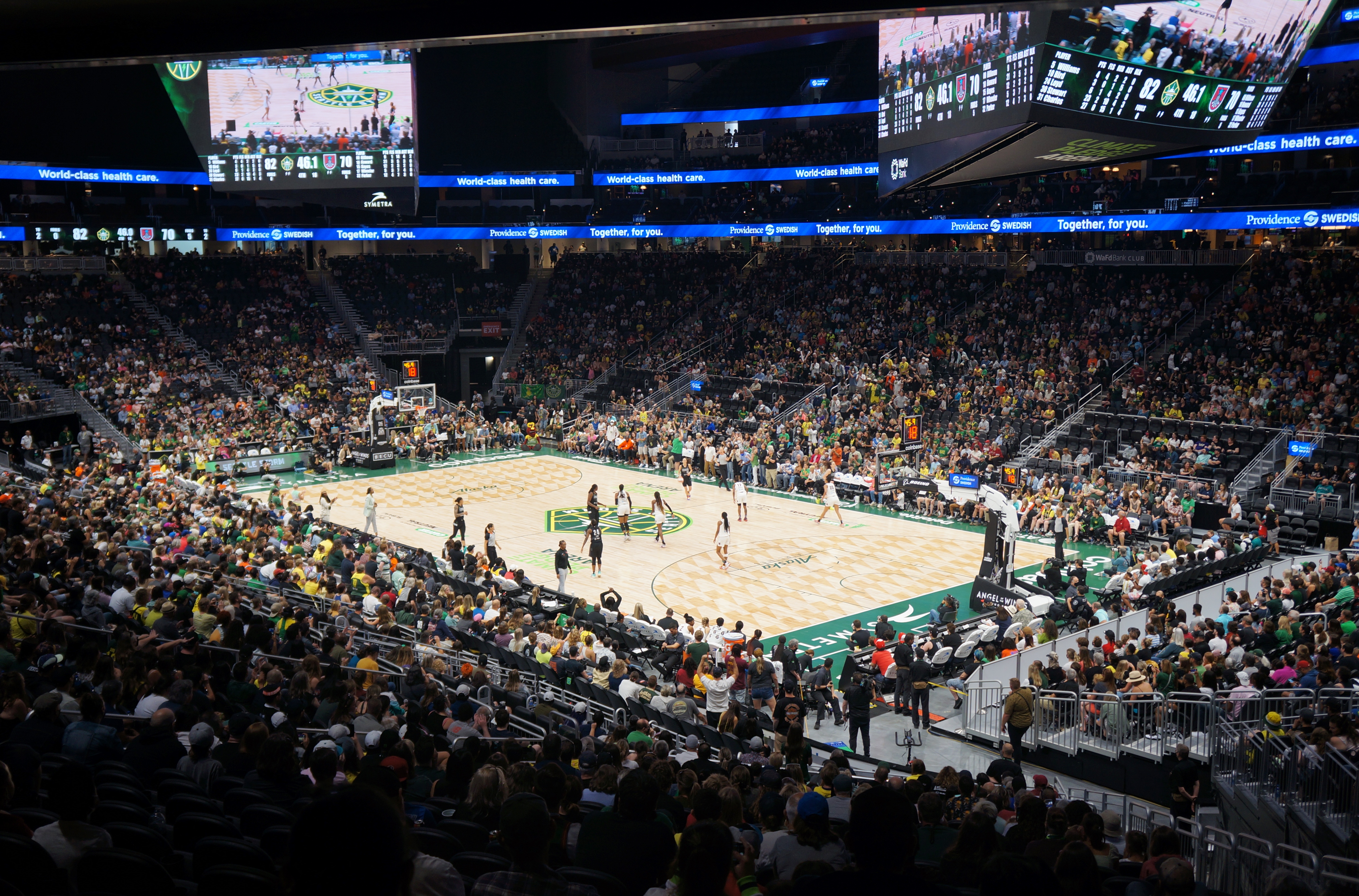 Wide interior view of a large arena filled with fans watching a basketball game on the court below.