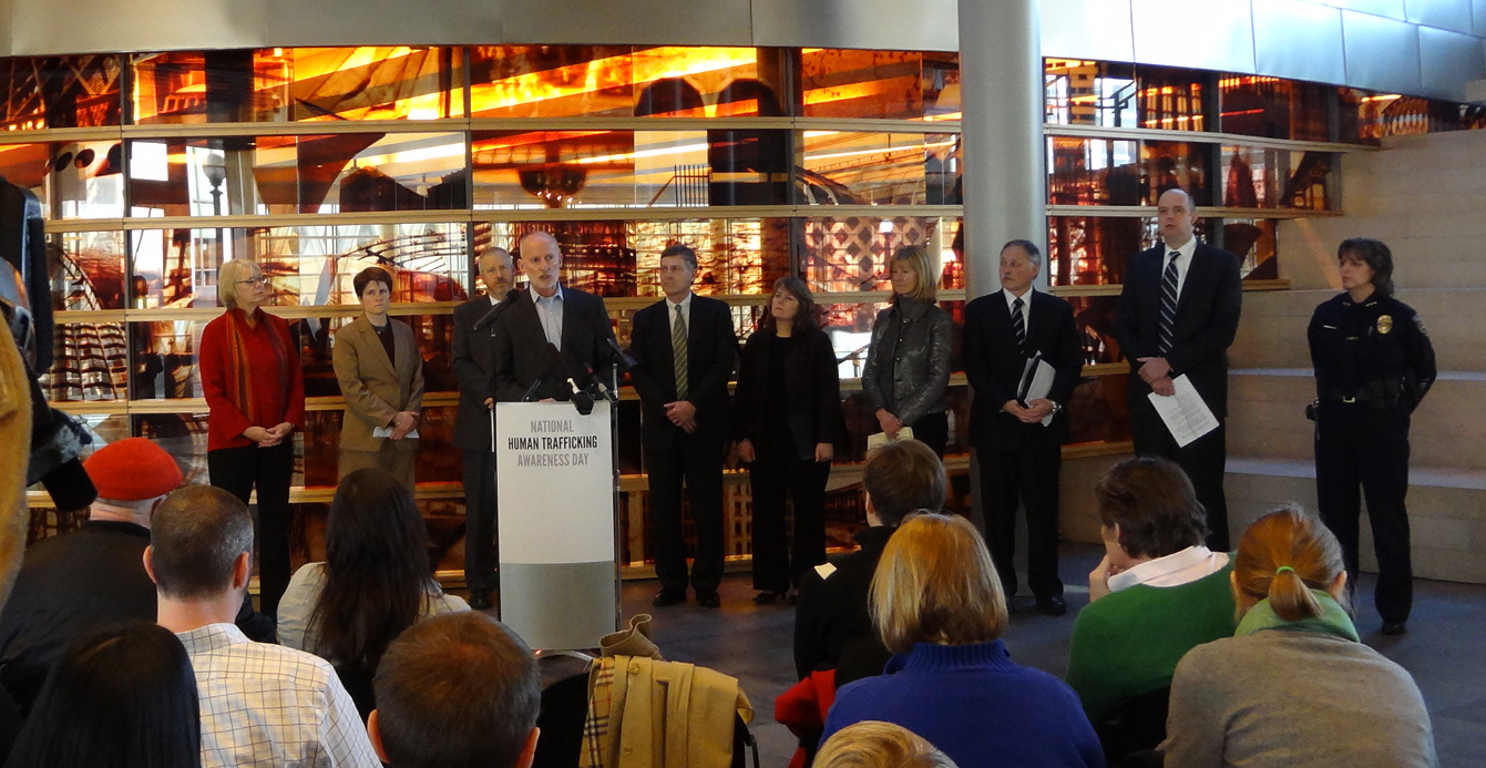 Officials and law enforcement officers stand at a podium at a Human Trafficking Awareness Day event.