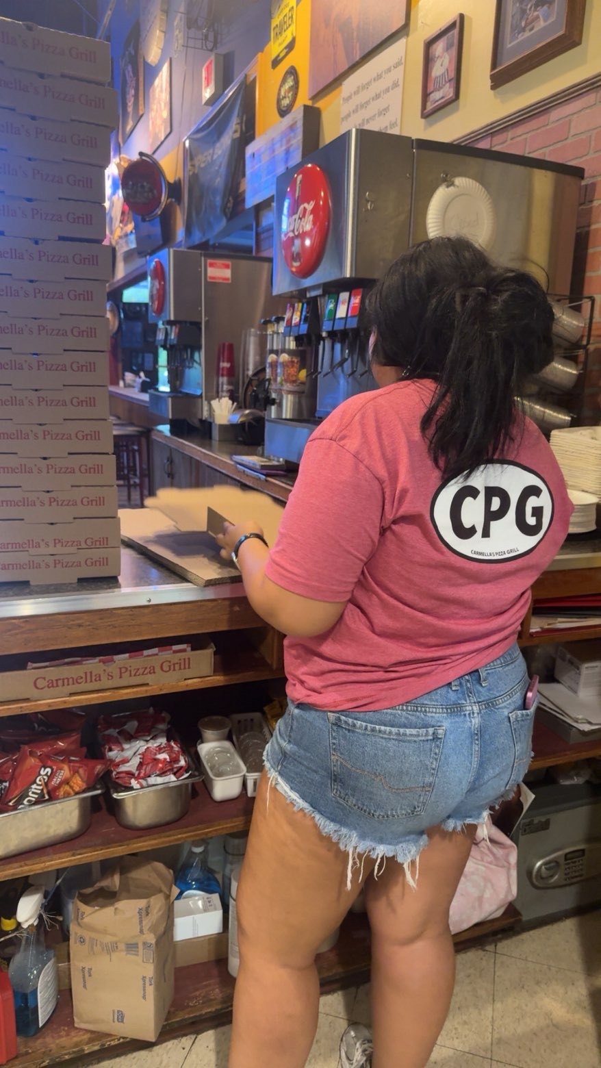 A worker in a pink restaurant shirt stands behind a service counter.