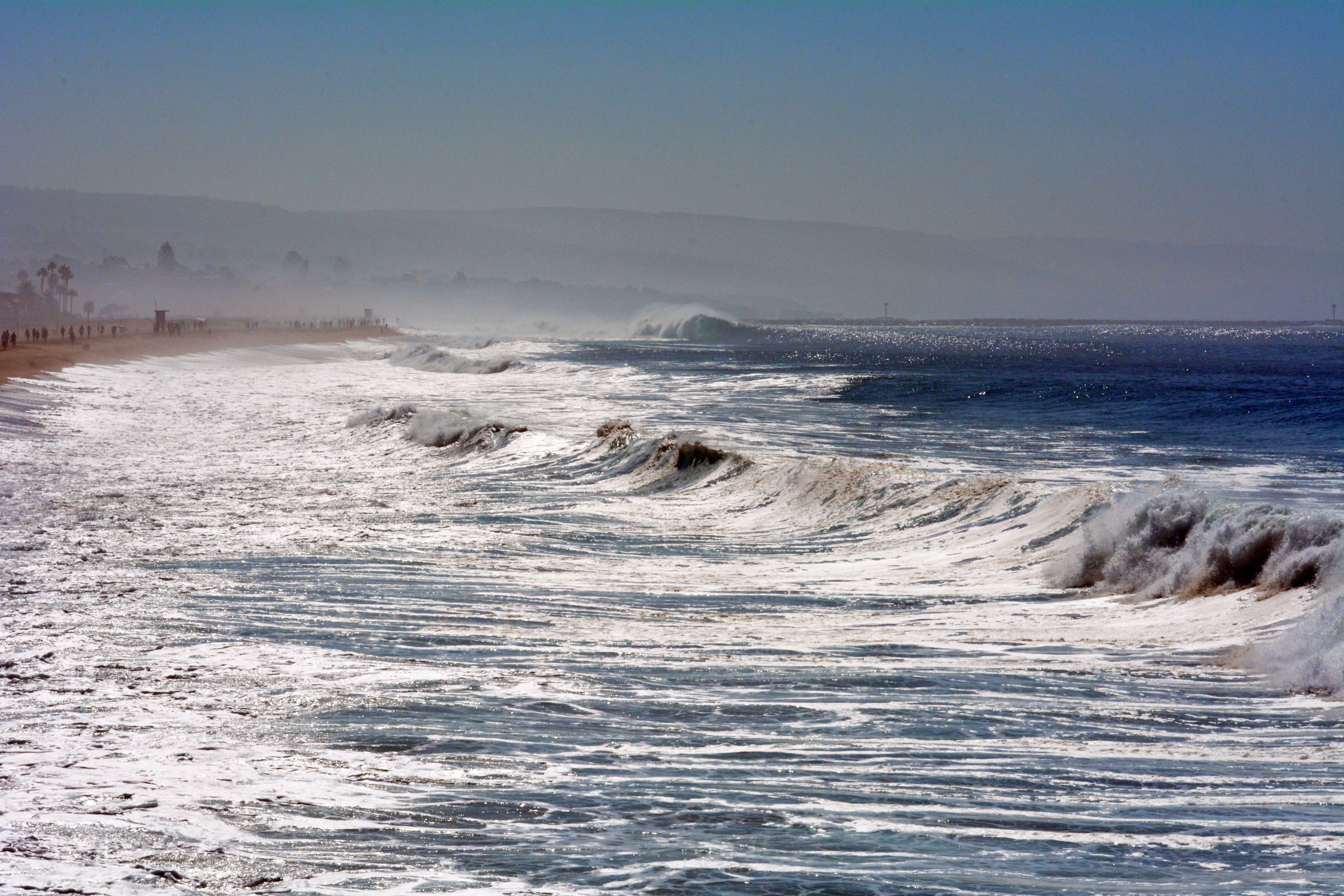 Large breaking waves crash along a sandy California shoreline.