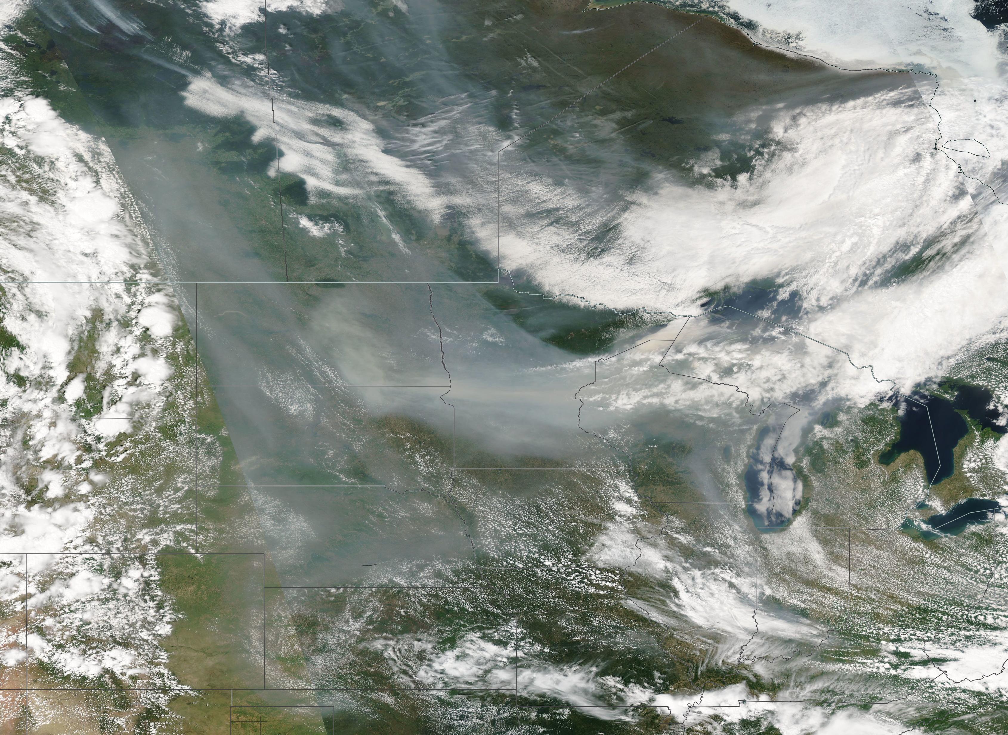 Satellite image showing a large brownish-gray wildfire smoke plume drifting across a wide geographic area.