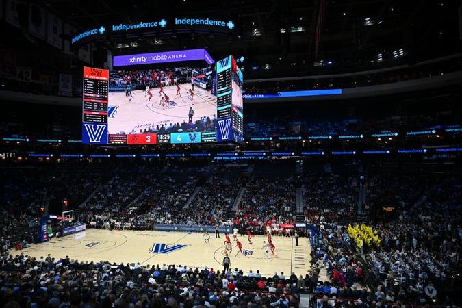 Interior of a basketball arena with a large center-hung scoreboard and crowd in the stands.