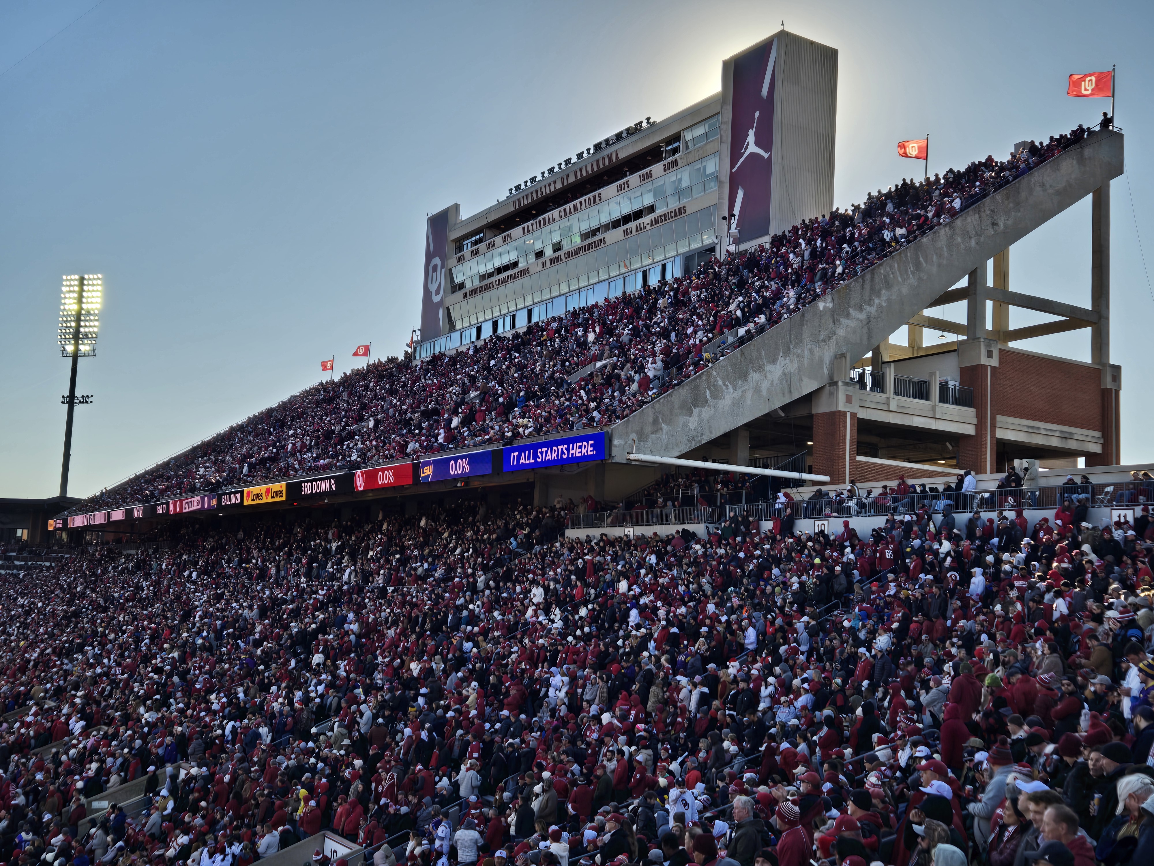 Packed stadium stands filled with fans in crimson and white during a college football game.