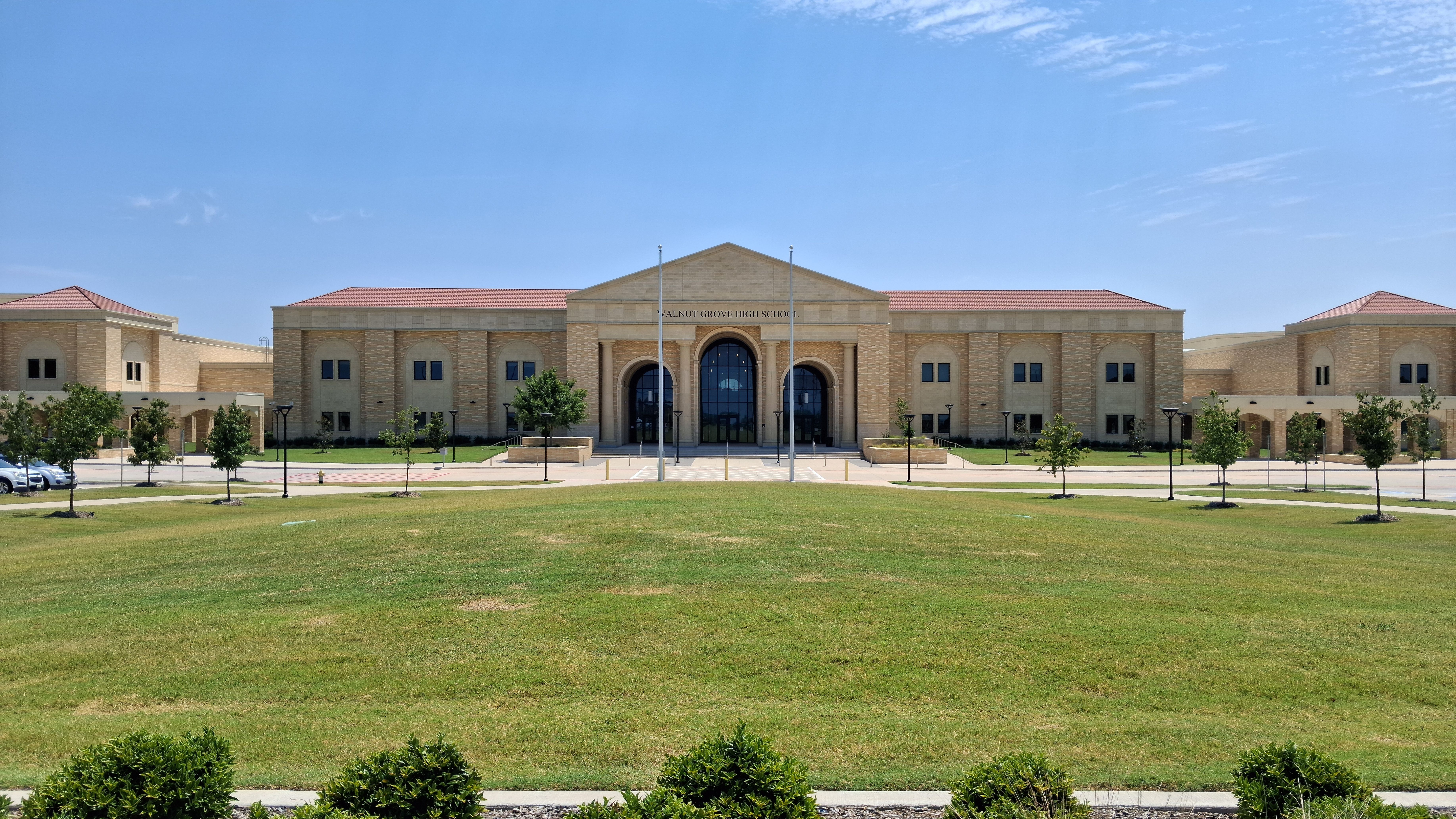 Large tan-brick high school building with red roof trim and a wide green lawn.