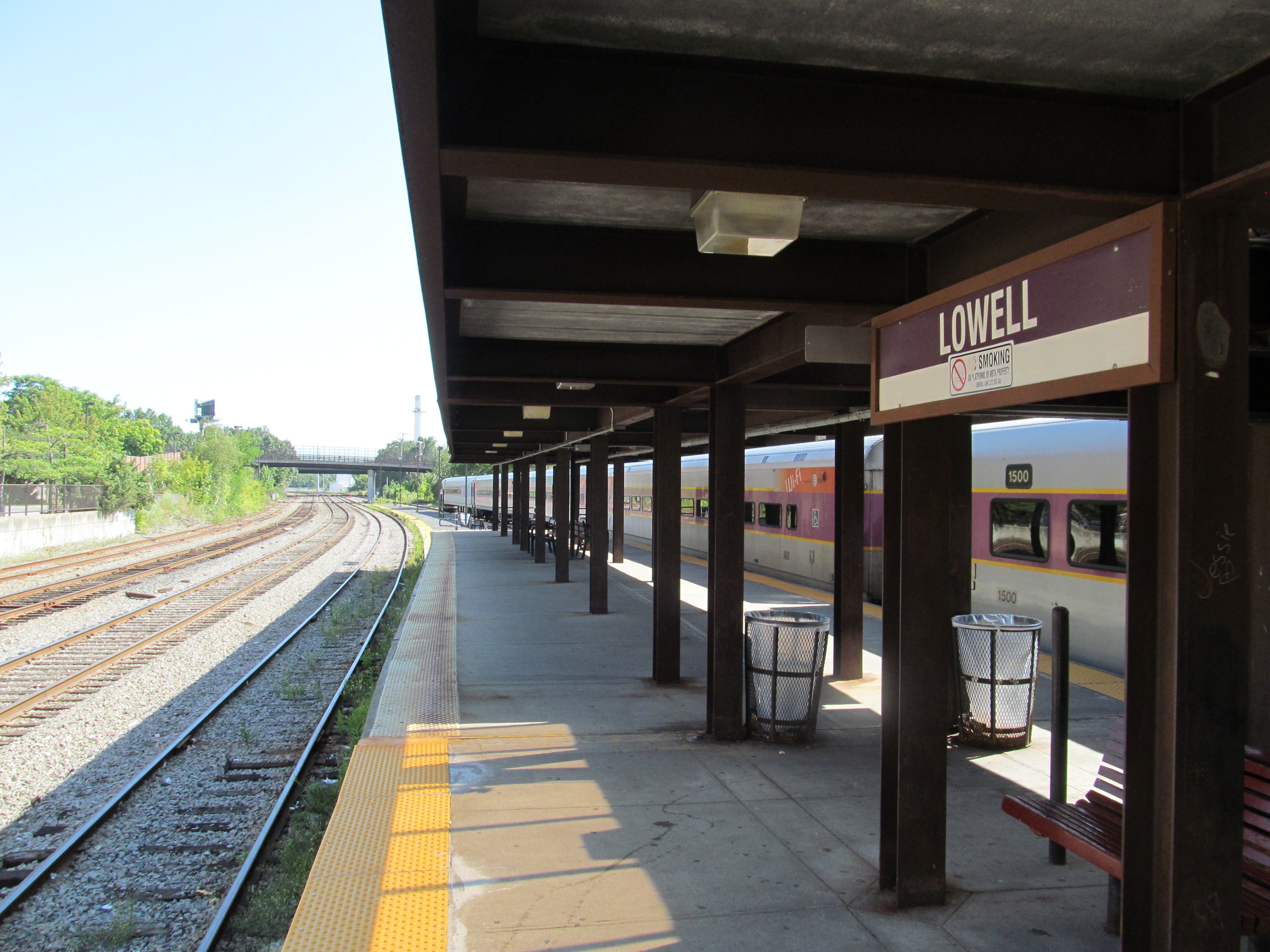 MBTA commuter rail coaches stopped at a station platform with railroad tracks alongside.