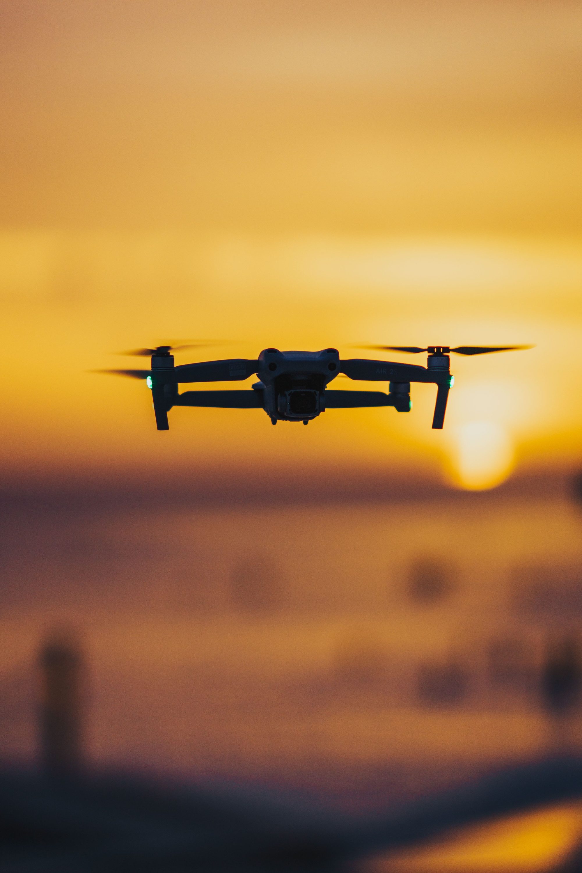 A drone flies over the ocean with a stunning sunset backdrop, casting a serene silhouette.