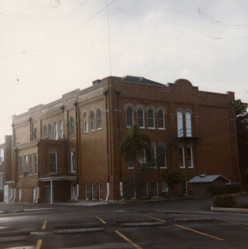 Two-story red brick school building with arched windows and an exterior metal staircase.