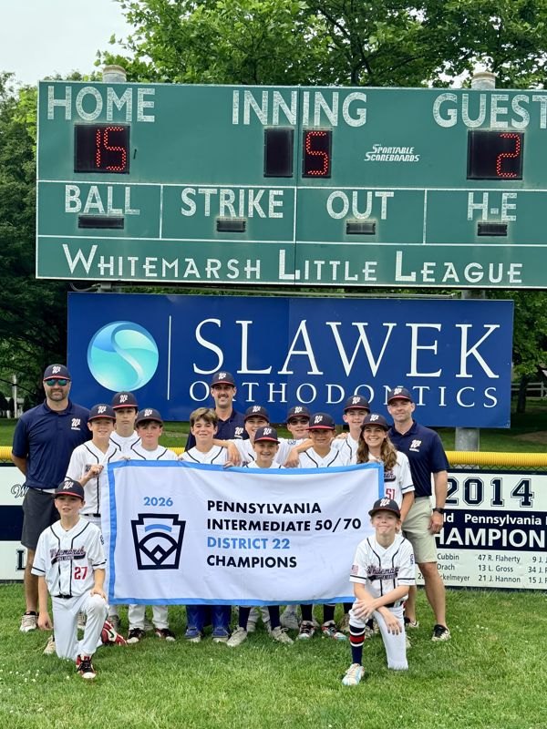 Youth baseball team posing with a District 22 championship banner in front of a scoreboard.