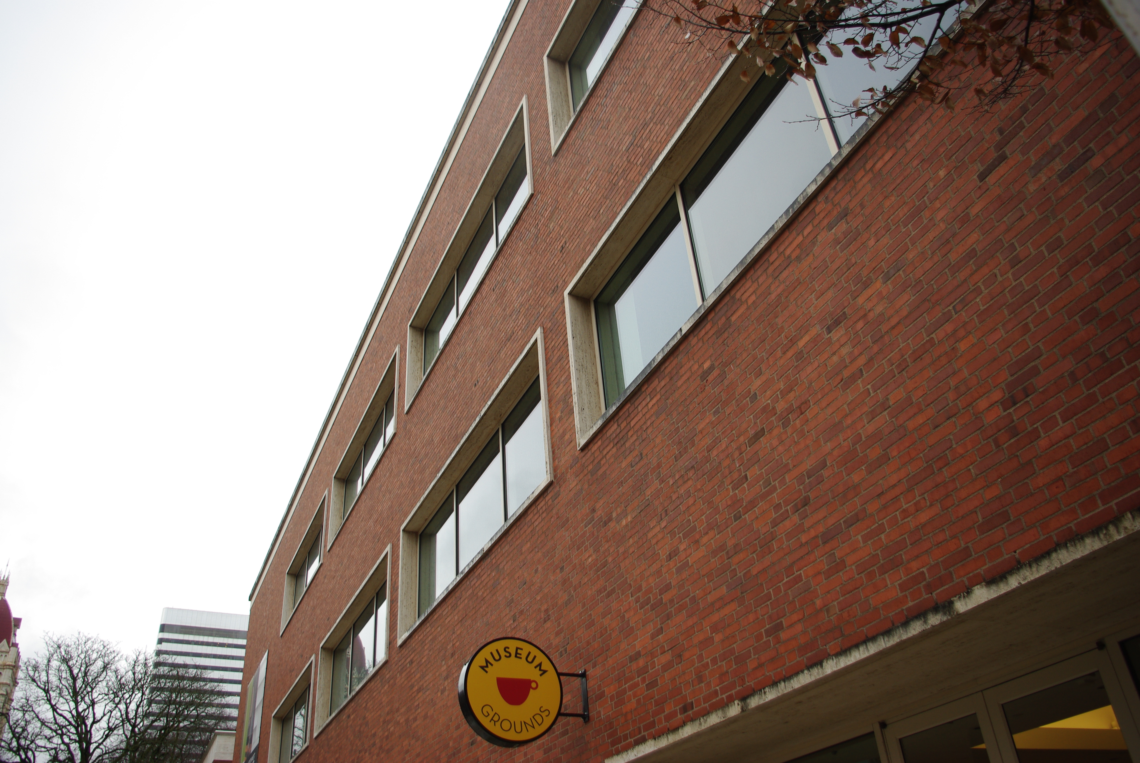 Red brick building exterior with rows of rectangular windows and a circular sign reading Museum Grounds.