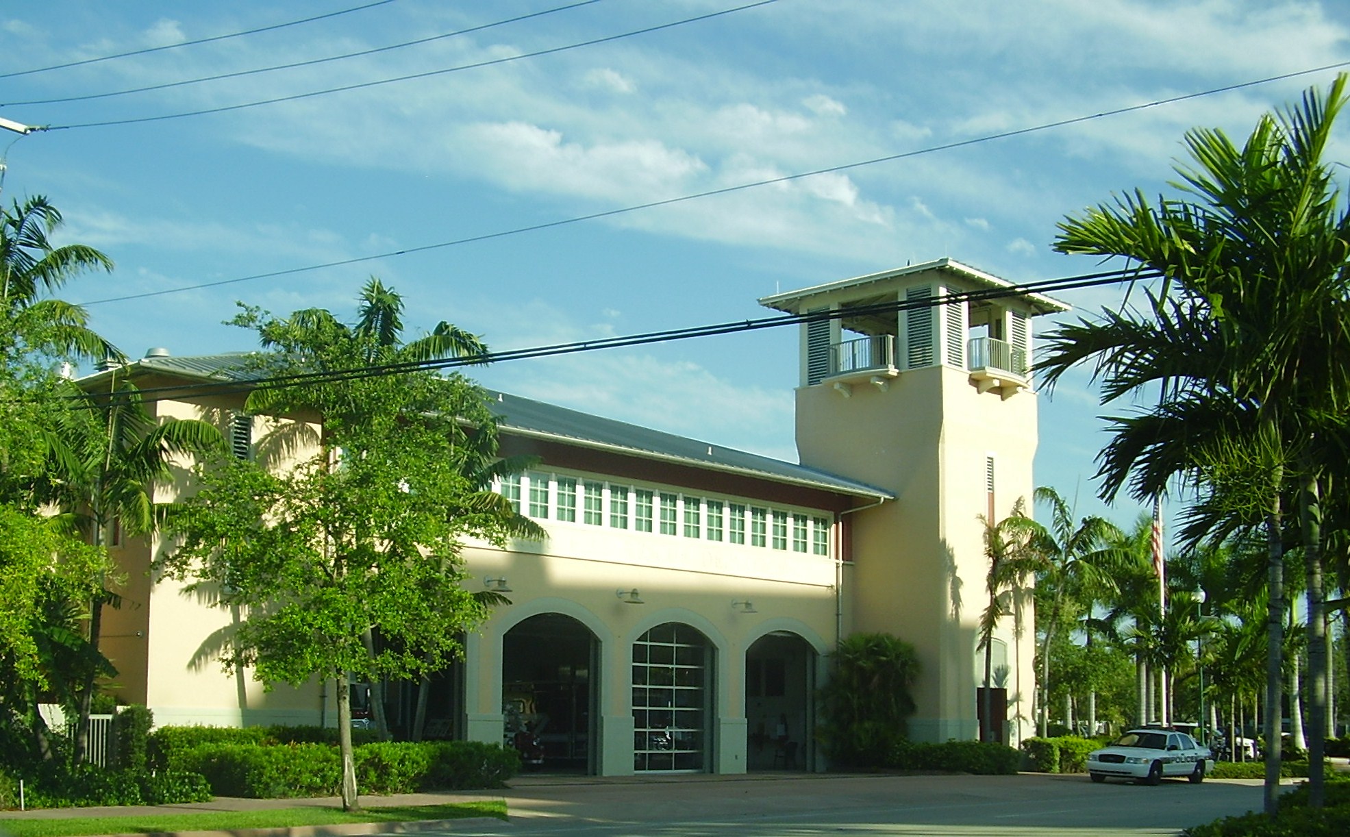 A beige fire station building with arched garage doors surrounded by palm trees.