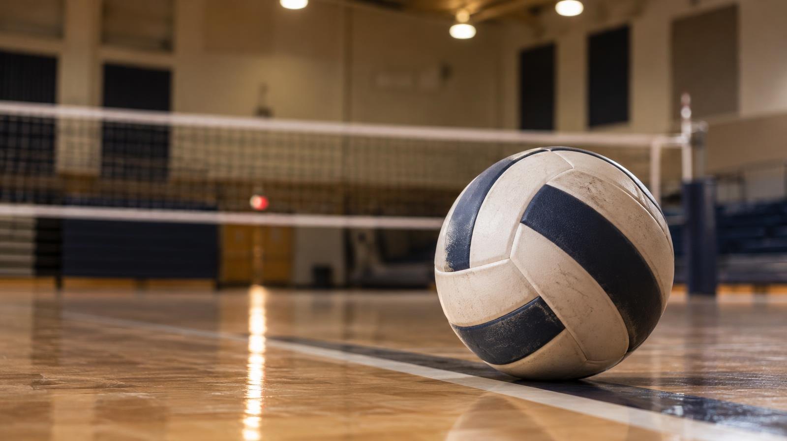 A volleyball on a hardwood gym floor with a net visible in the background.