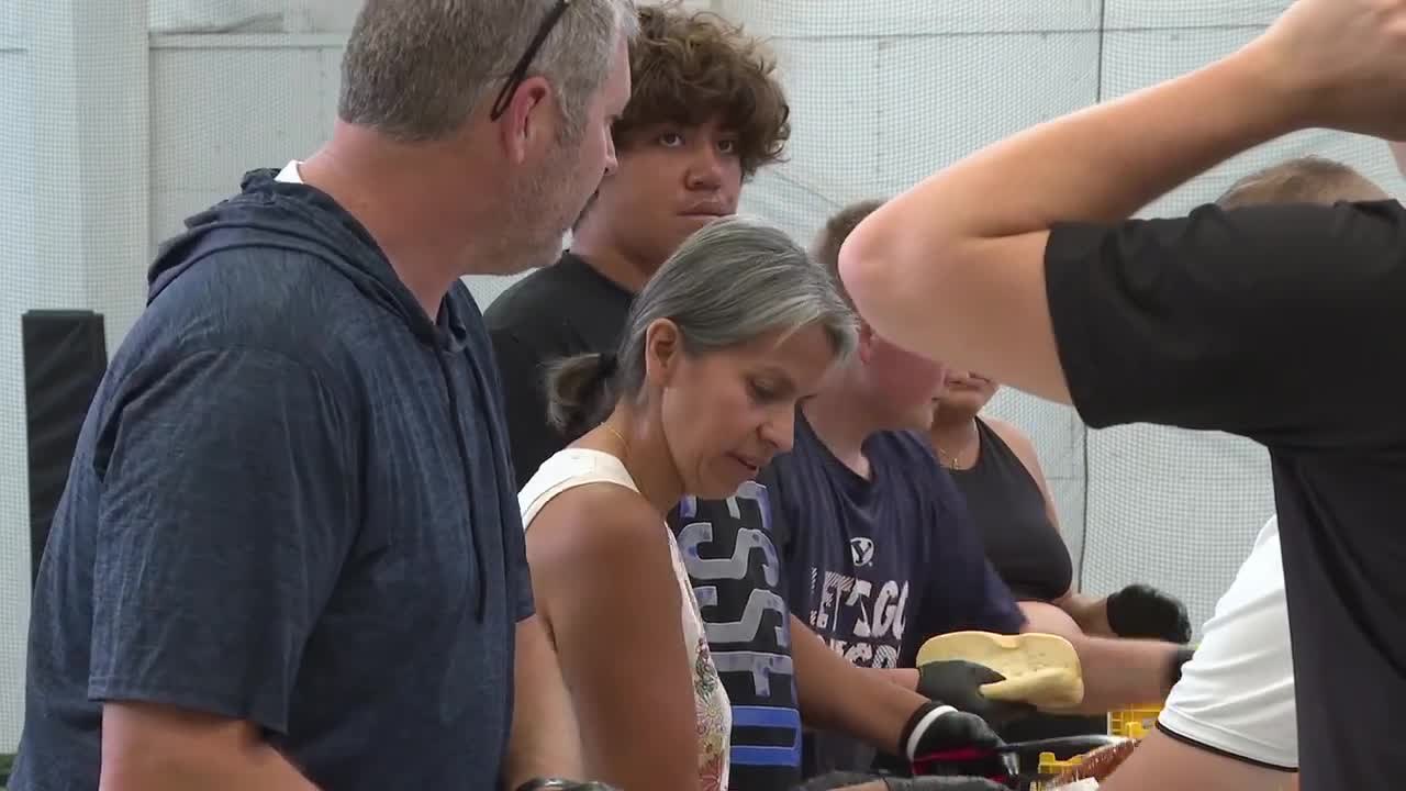 A group of adults and teenagers stand around a table indoors distributing supplies in a gymnasium.