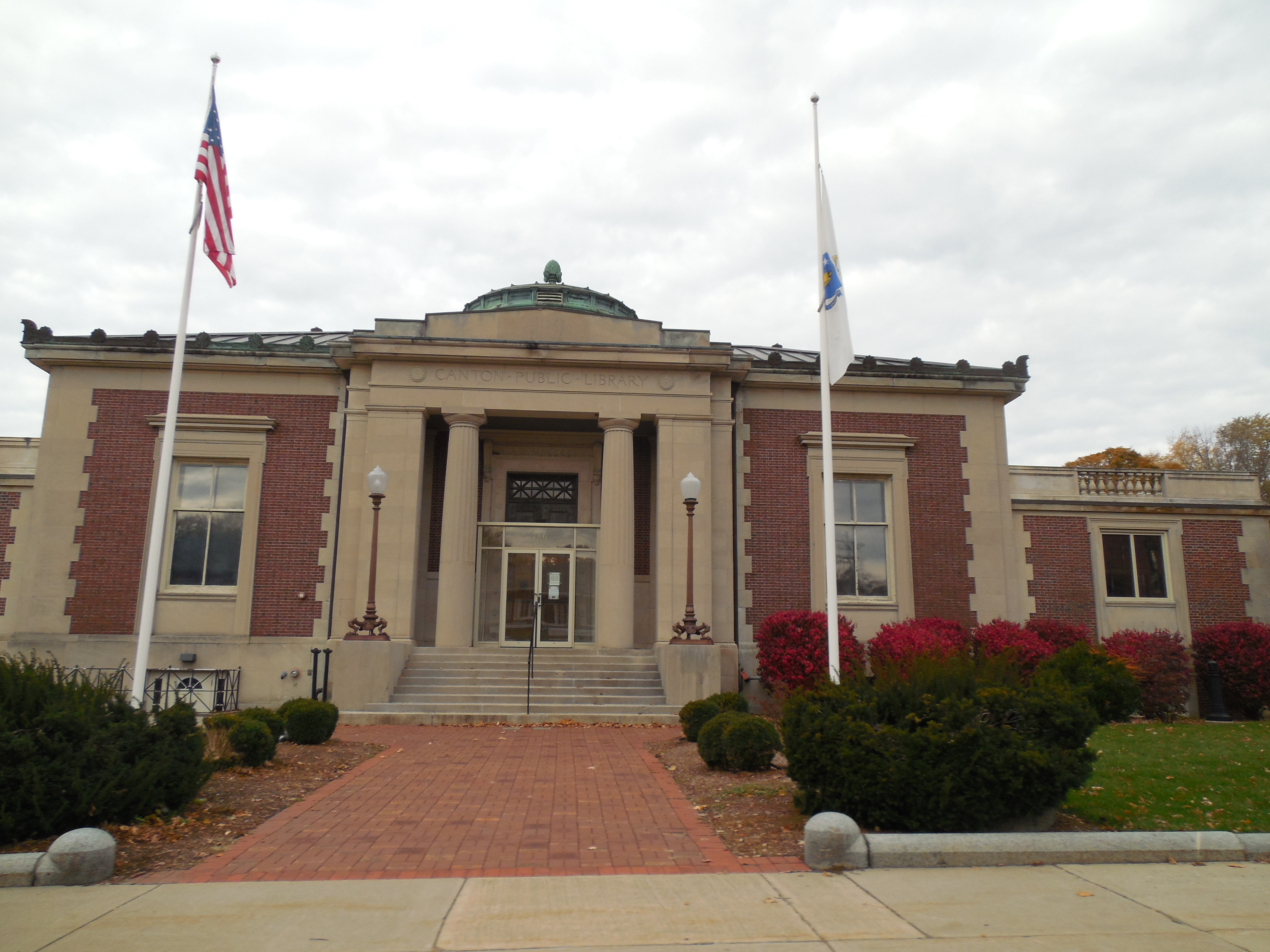 Neoclassical brick library building with columned entrance, green dome, and two flagpoles.