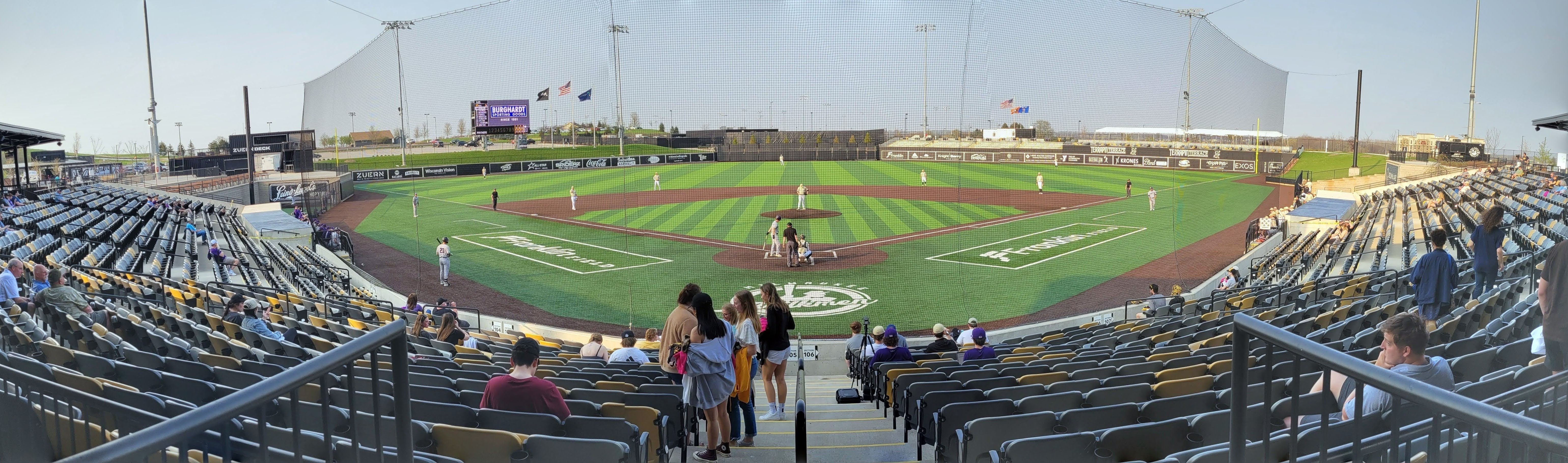 Panoramic view of a baseball stadium with green turf, red warning track, and scattered fans in the stands.