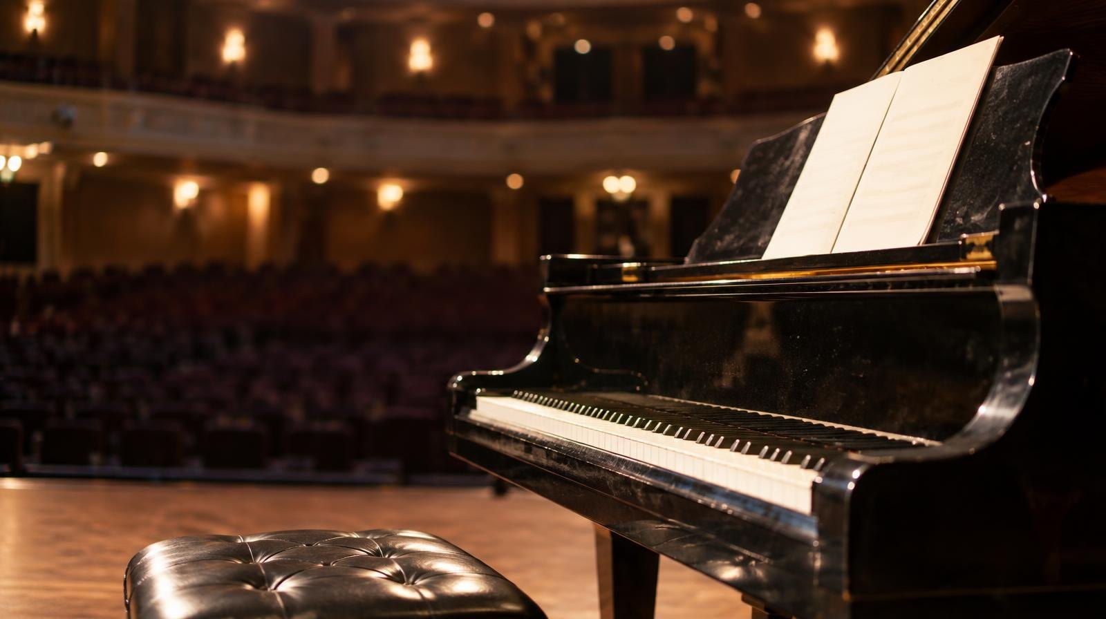 A grand piano on a concert stage illuminated by a warm spotlight.