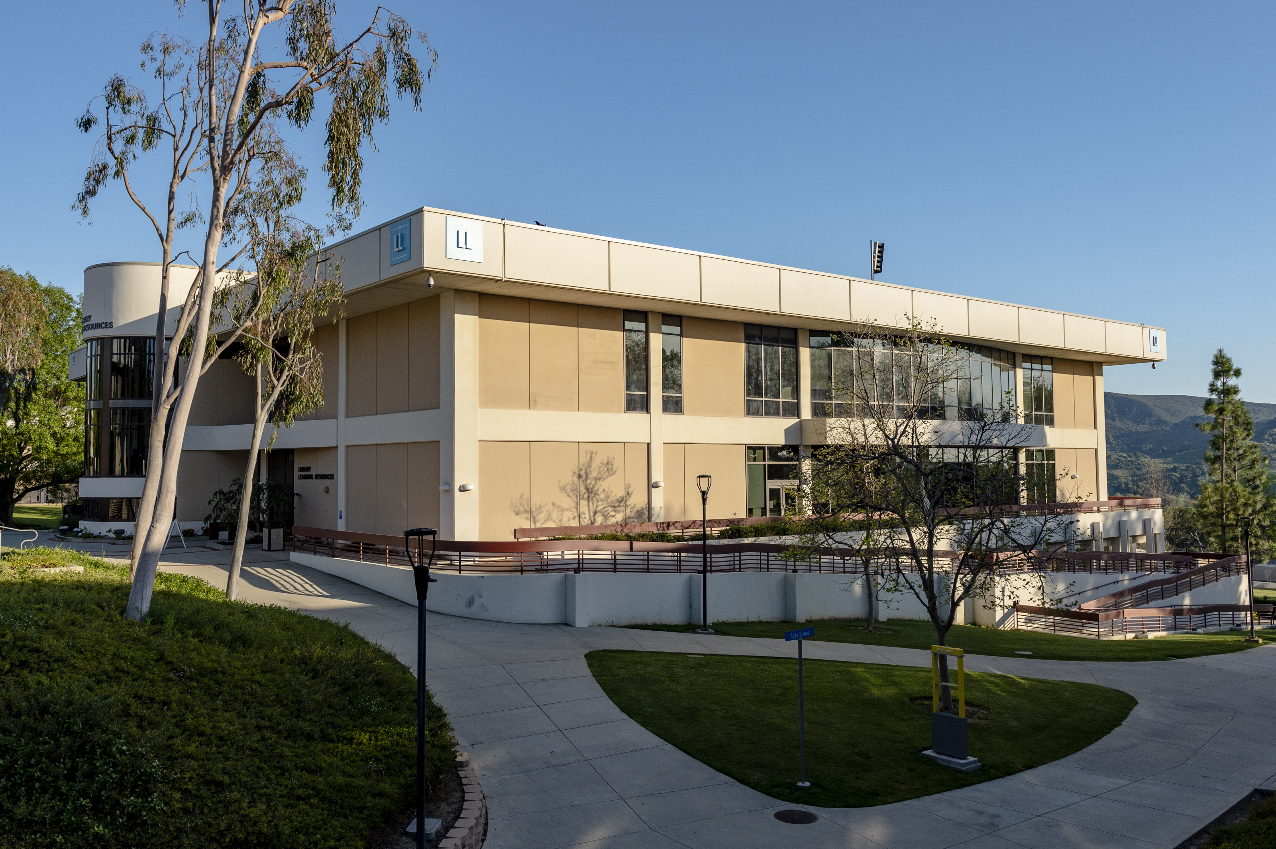 Two-story modern tan campus building with large windows, walkways, and green lawn