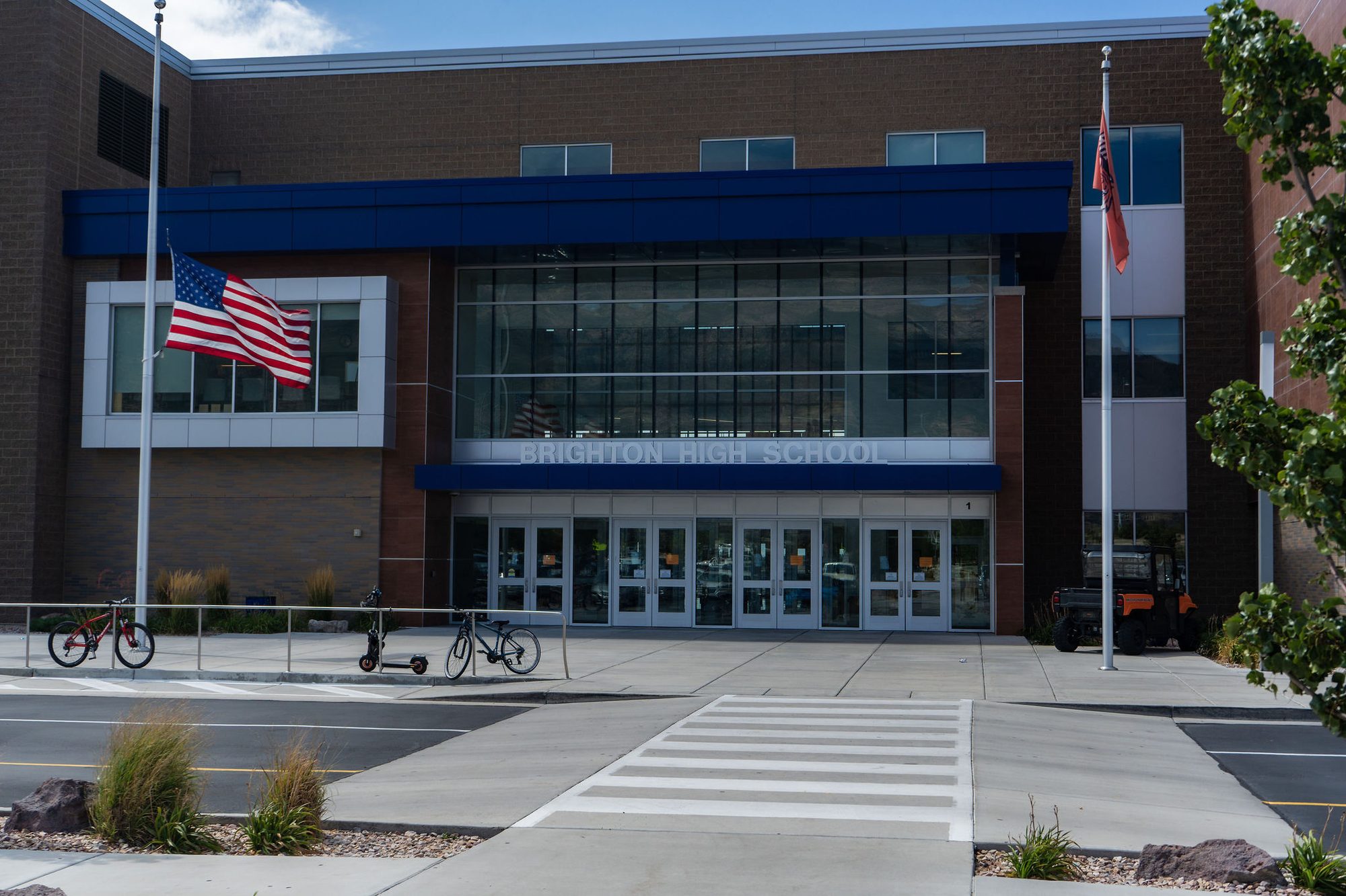 Modern brick-and-glass high school entrance with flags and school name above the doors.