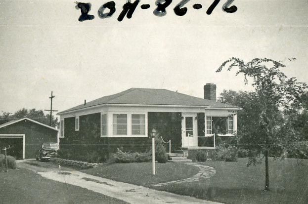 Black-and-white photo of a single-story ranch house with a front porch and garage.