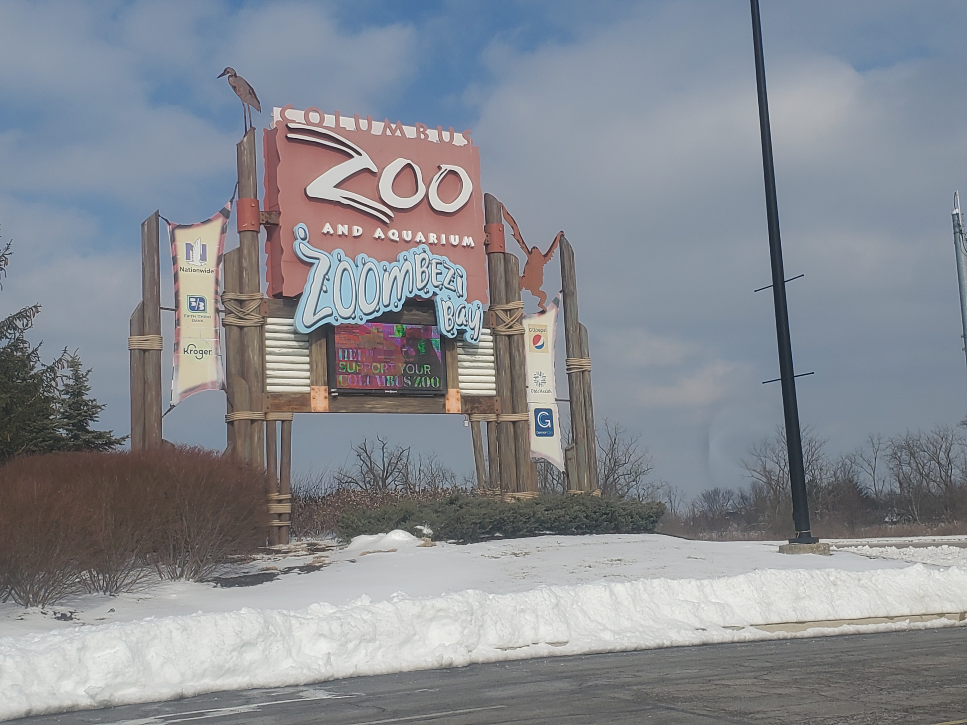 Large freestanding sign reading Columbus Zoo and Aquarium and Zoombezi Bay in a snowy setting.