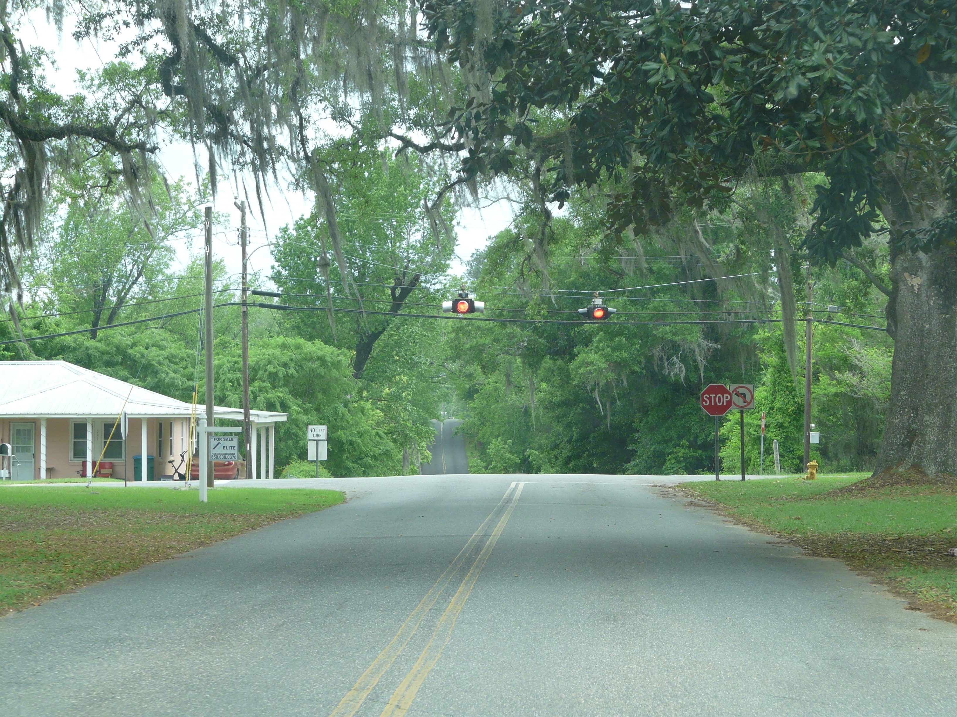 A two-lane road approaching a signalized intersection with red traffic lights and a stop sign.