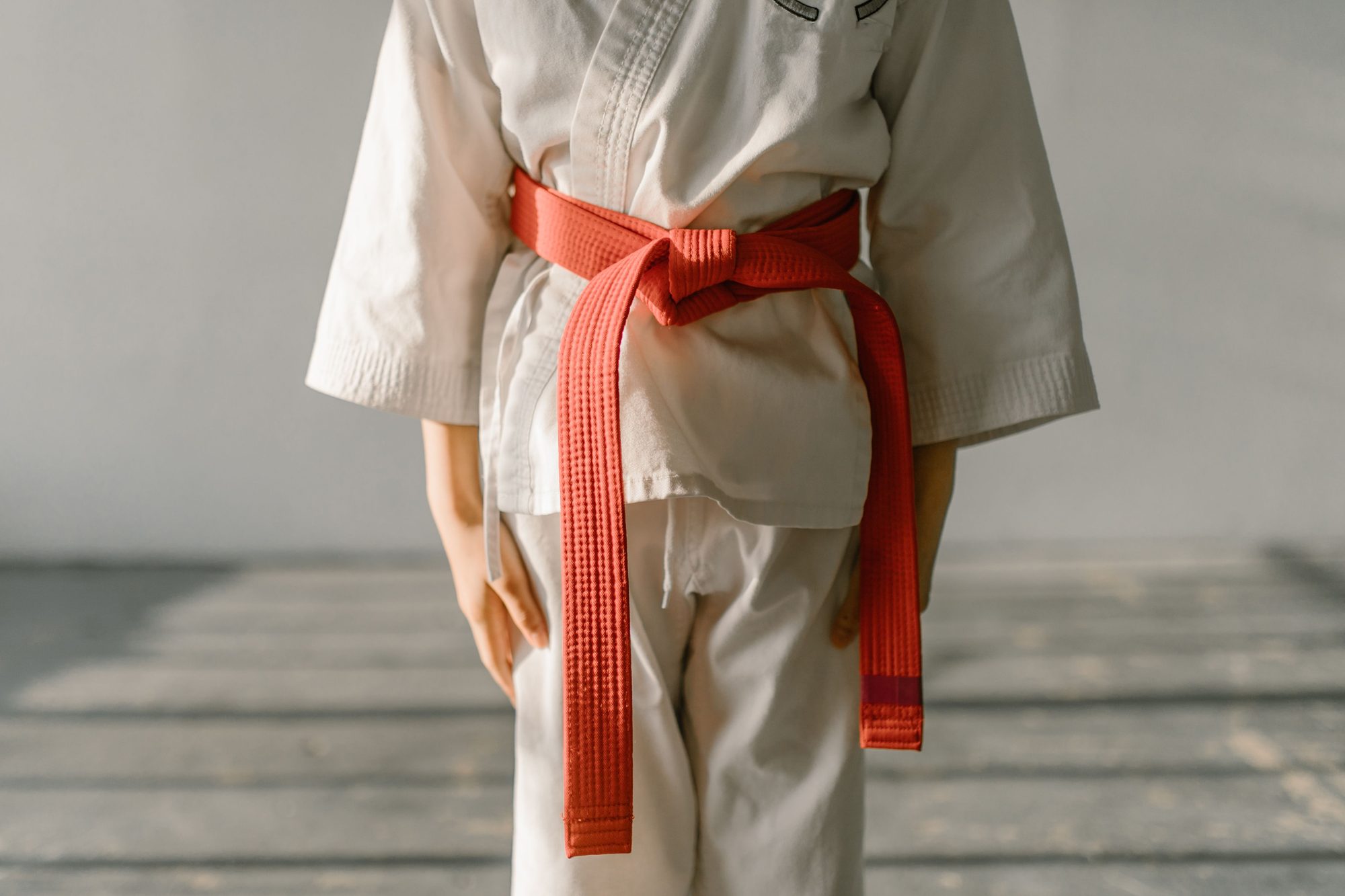 Close-up of a martial artist wearing an orange belt and white uniform, standing indoors.