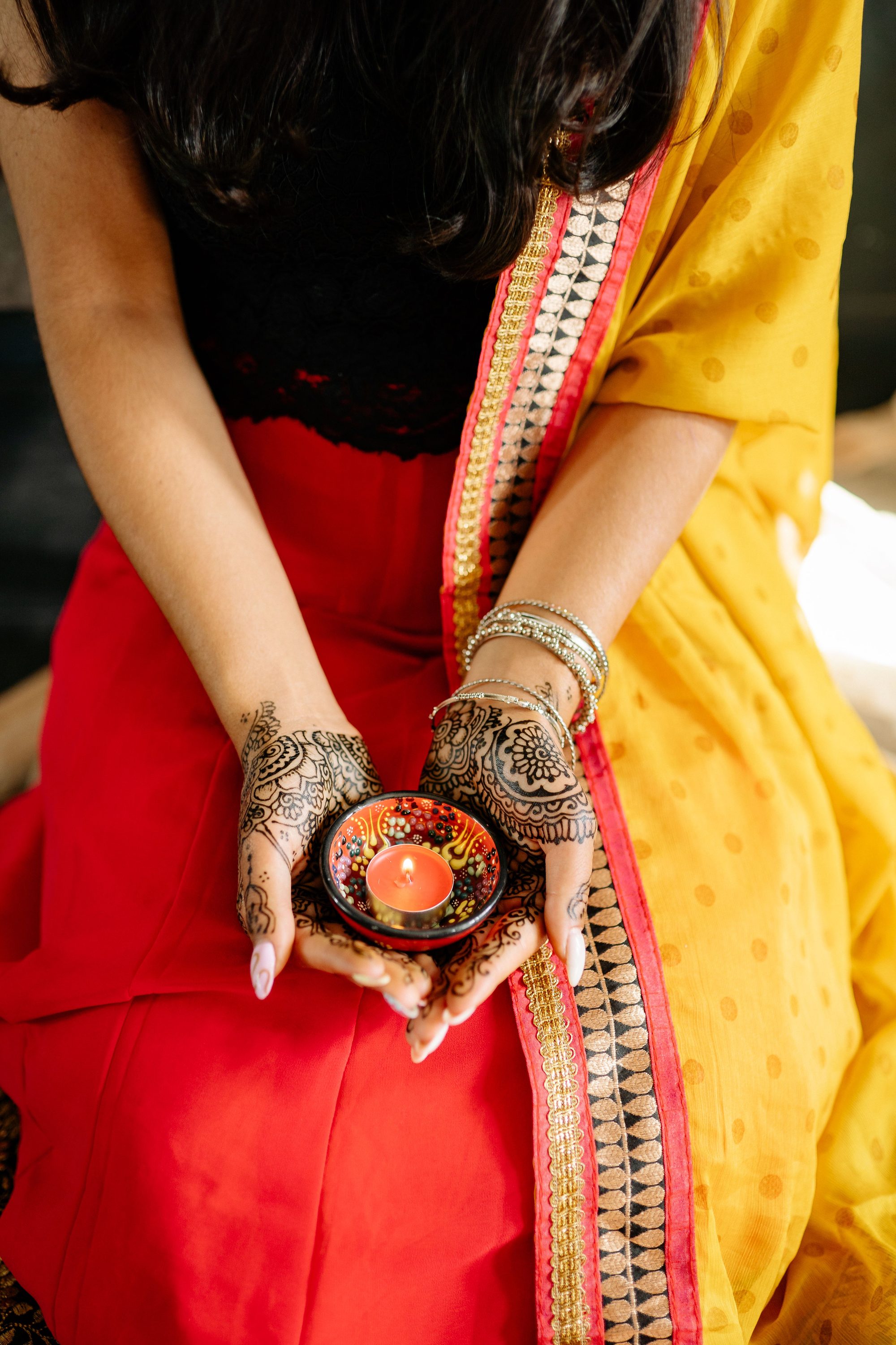 Close-up of hands with henna holding a candle, celebrating Diwali indoors.