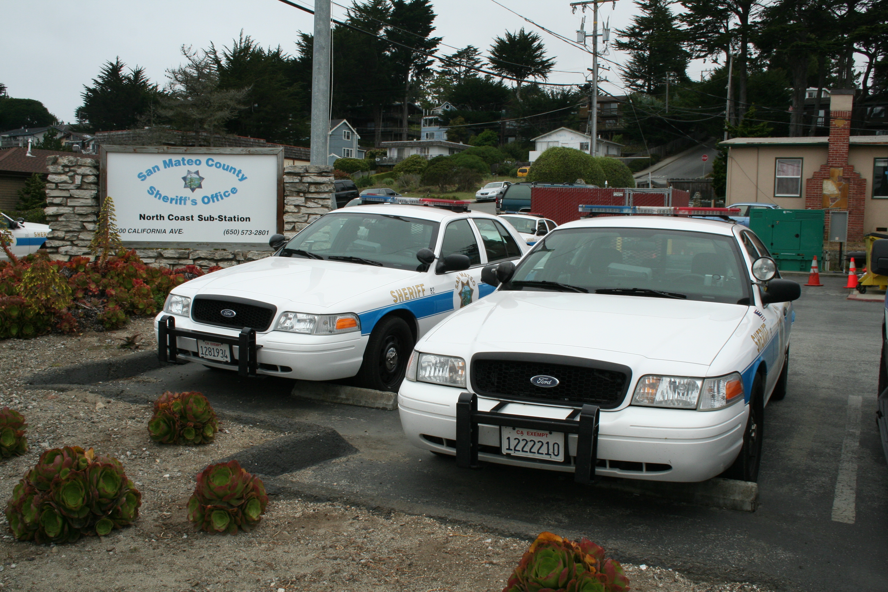 Two white sheriff's patrol cars parked in front of a stone sub-station sign.