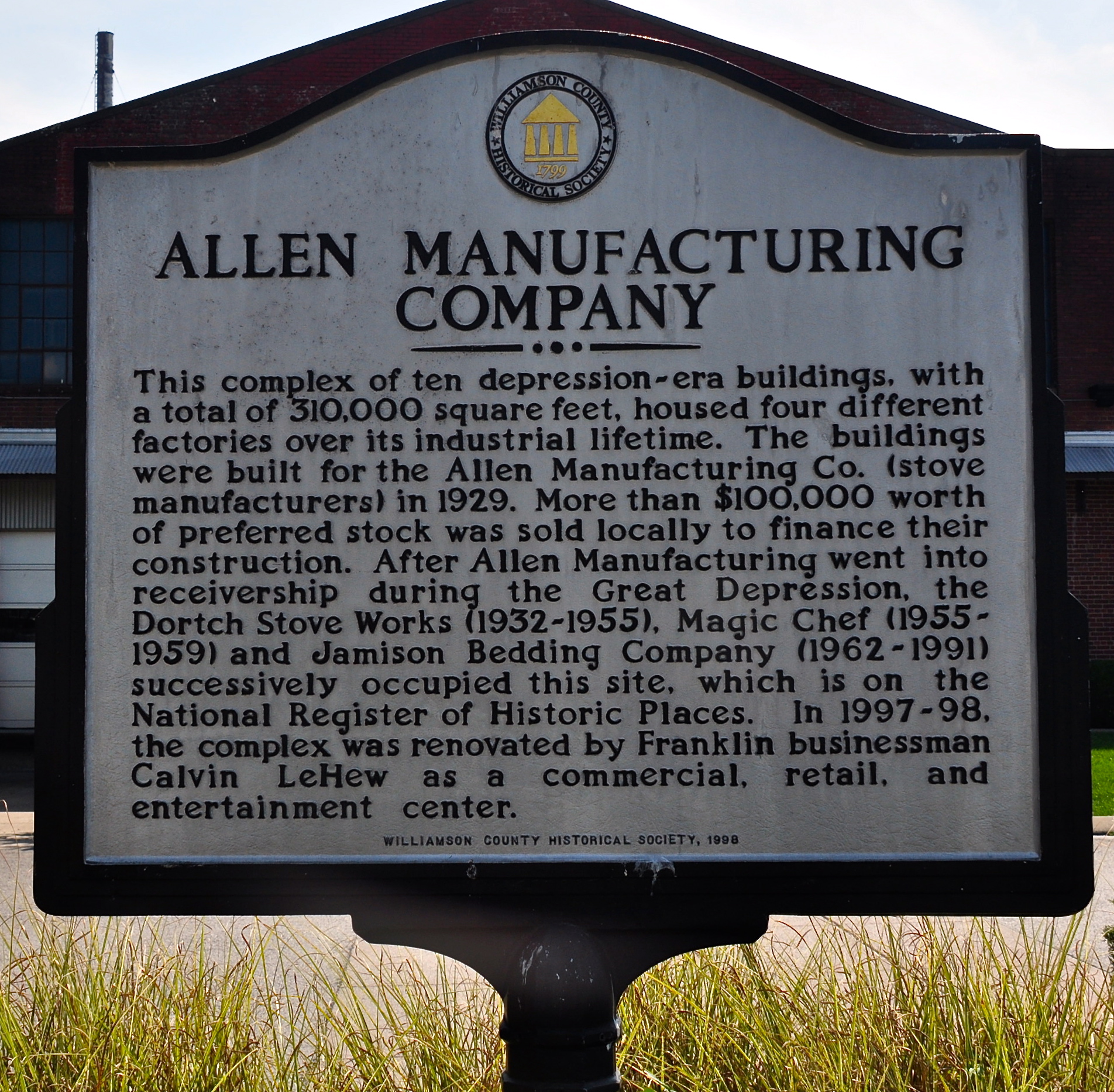 Historical marker sign mounted on a post in front of a brick building.