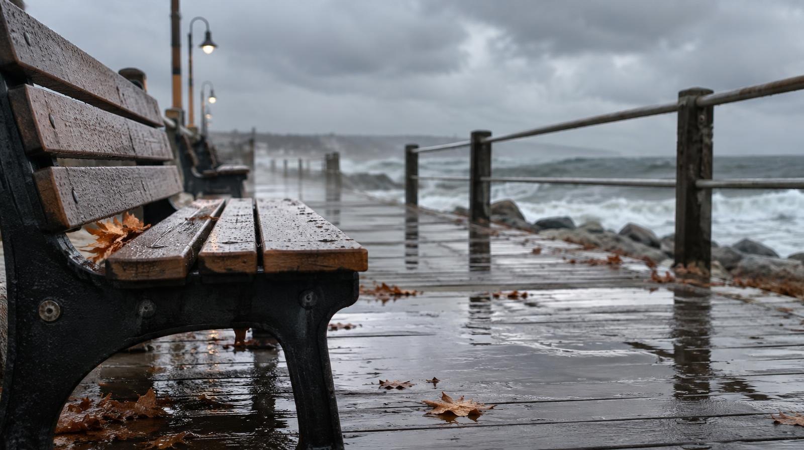 Rain-soaked boardwalk with puddles reflecting grey stormy skies and waves in the background.