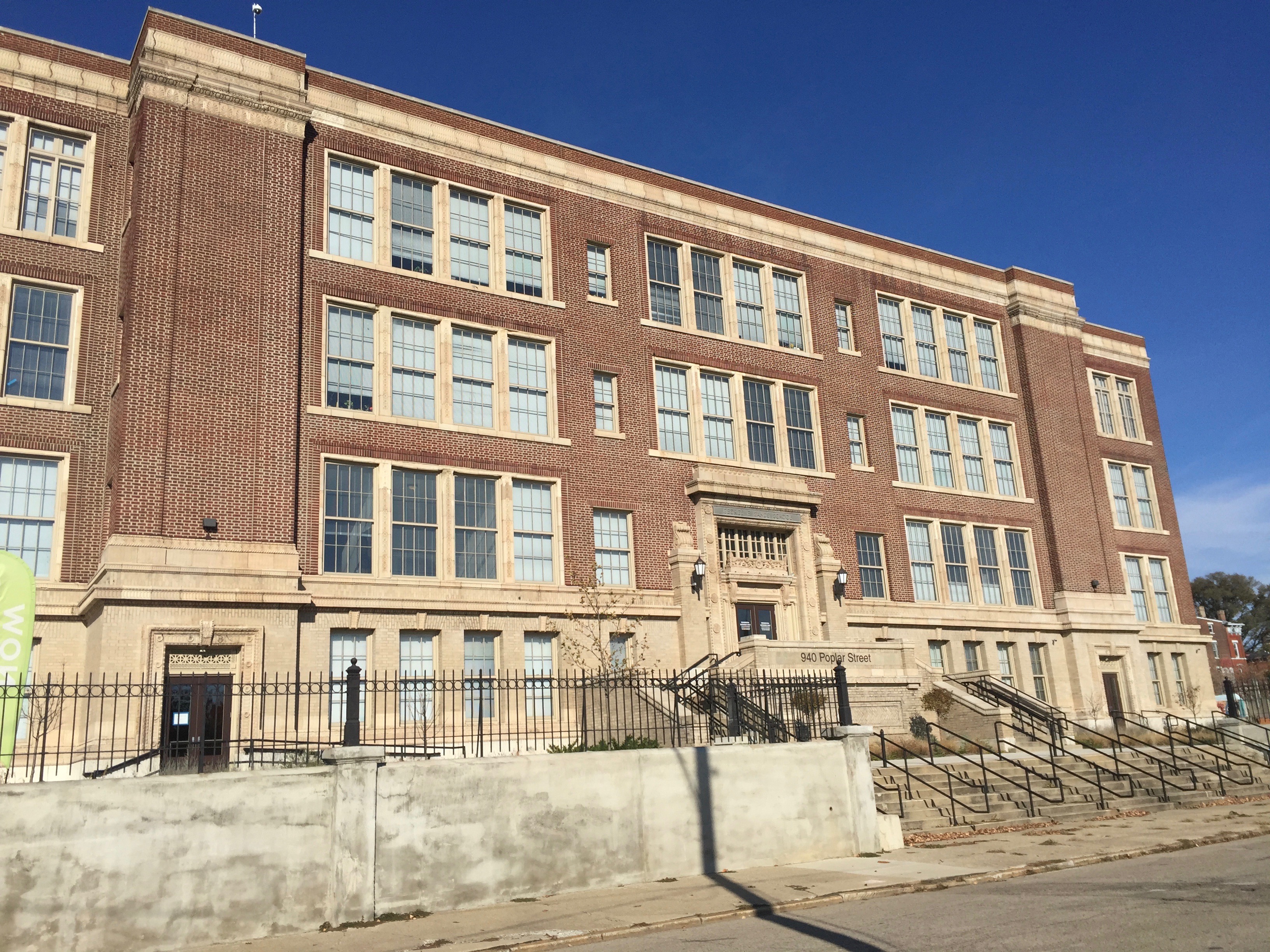 A large brick former school building with stone trim and exterior entrance stairs.