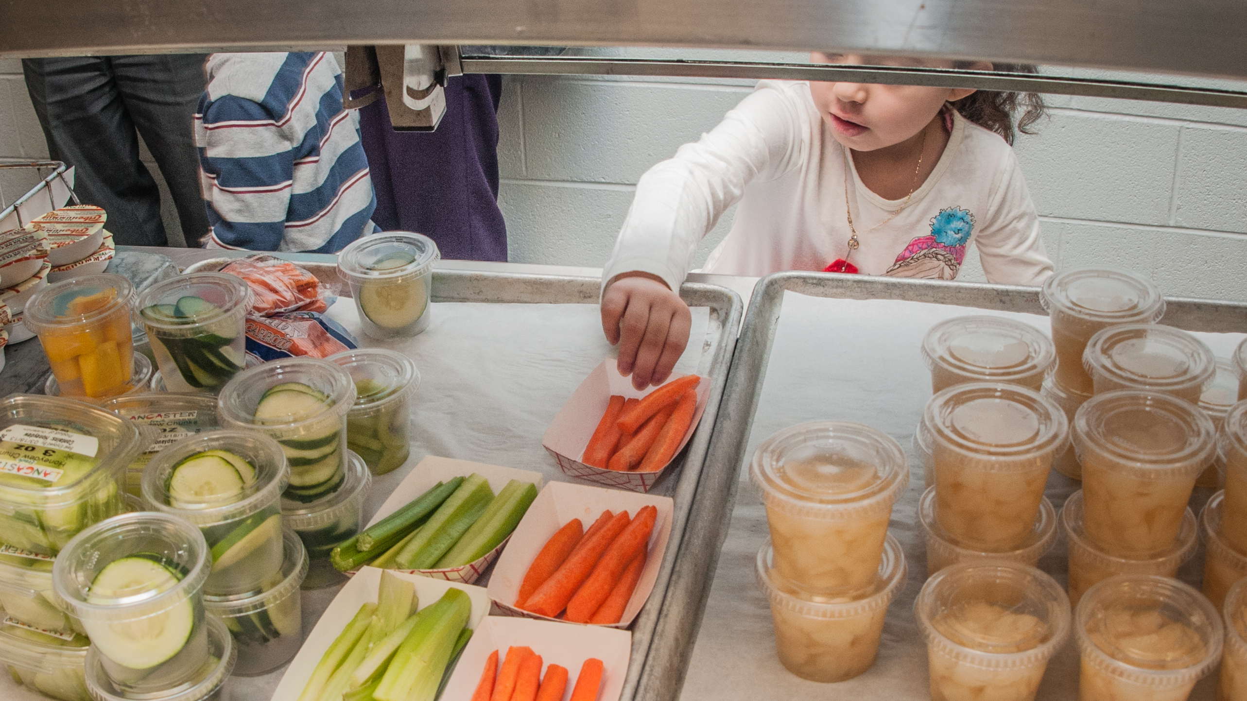 A child reaches for a carrot at a school cafeteria vegetable serving station.