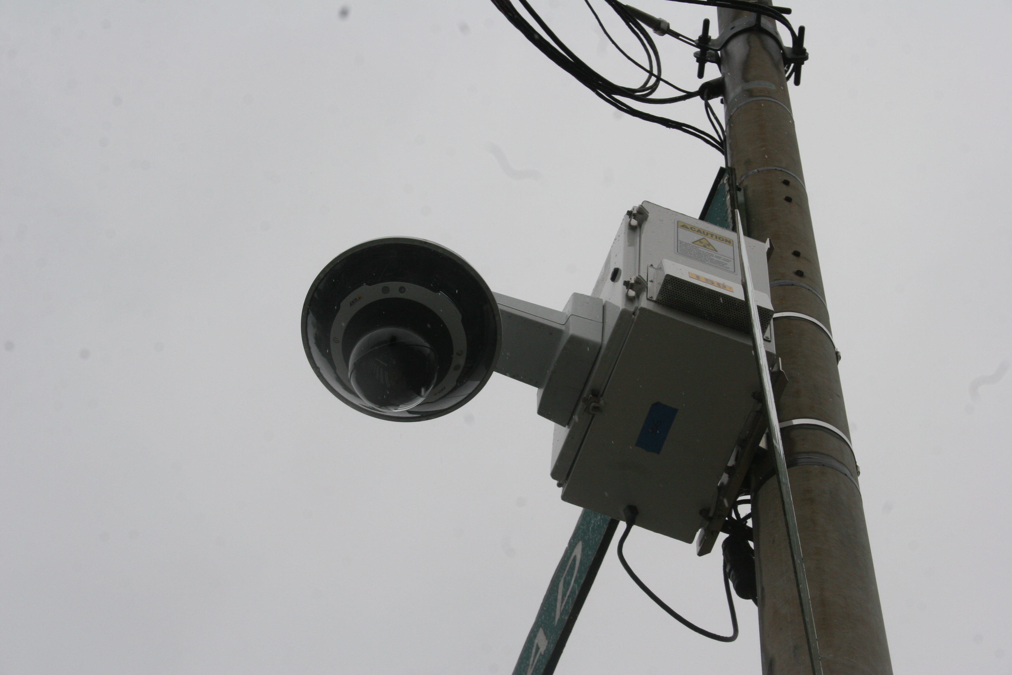 Dome-style surveillance camera mounted on a utility pole against an overcast sky.