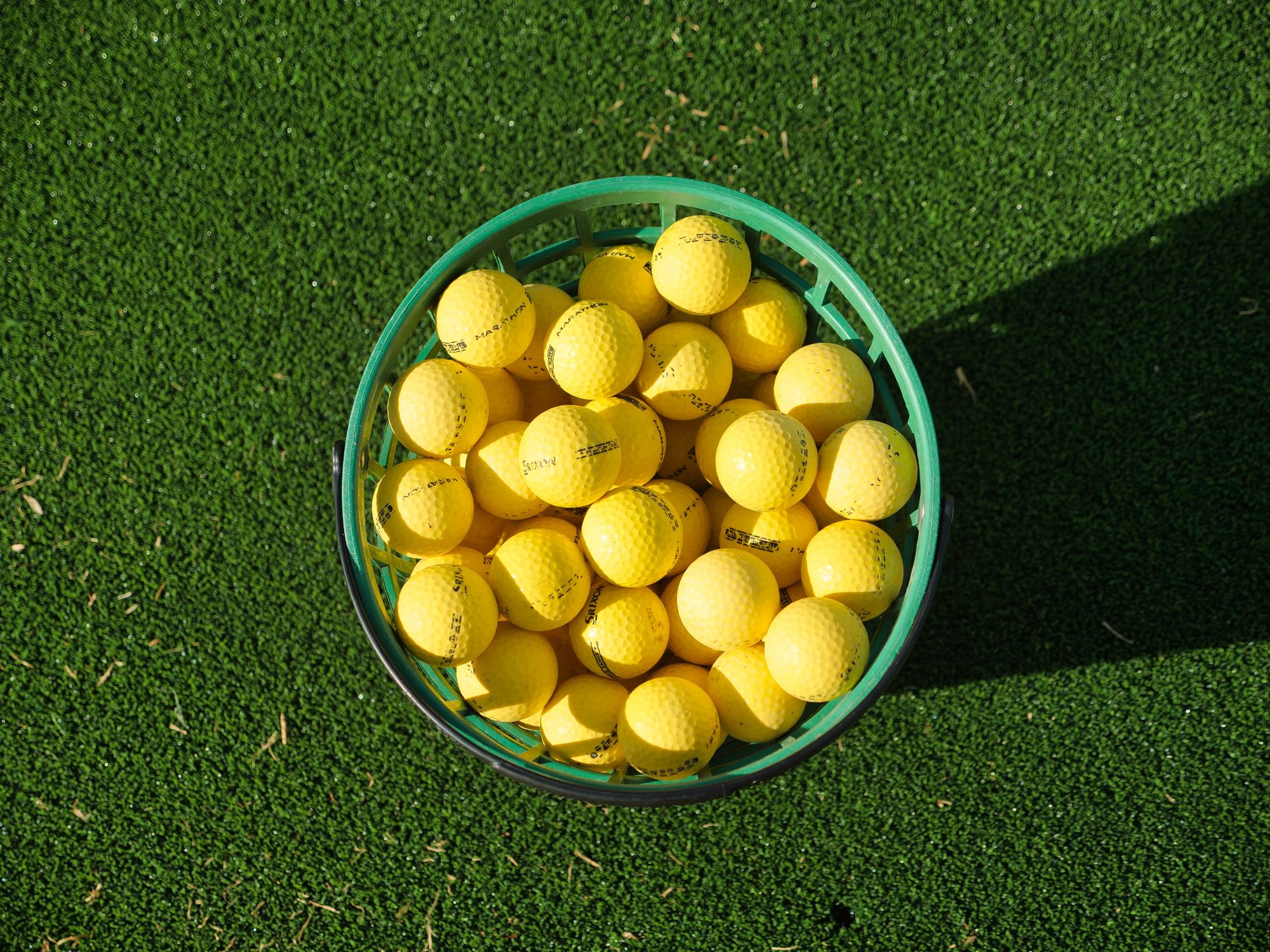 Top view of a basket filled with yellow golf balls placed on bright green artificial turf.