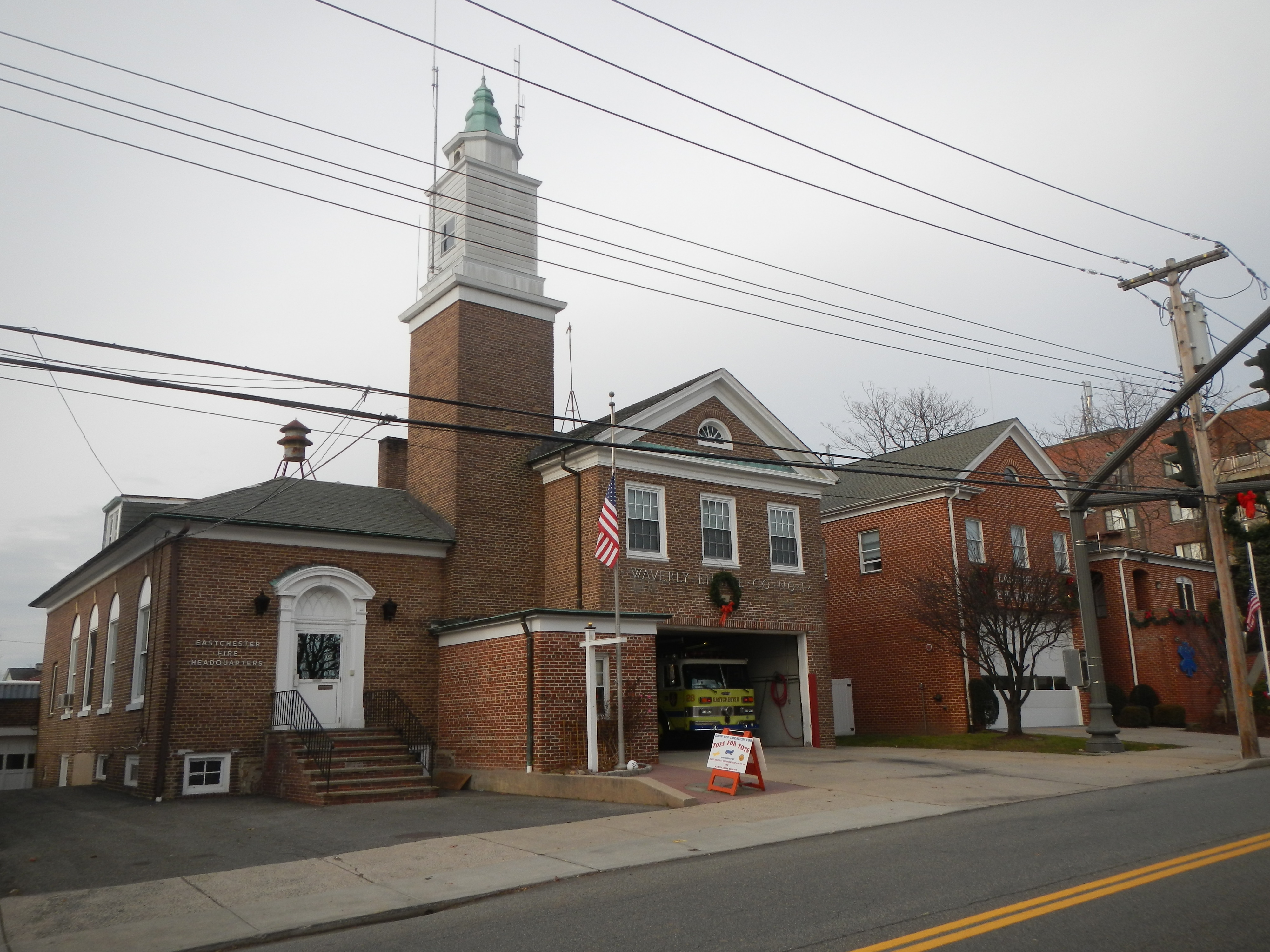 Brick firehouse on a street corner with an American flag and open apparatus bay.