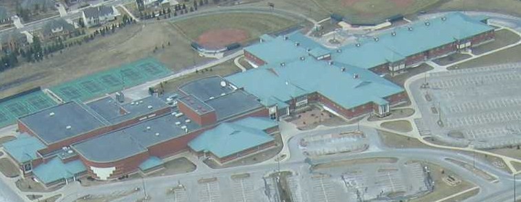 Aerial view of a large school campus with brick buildings, teal roofs, and tennis courts.