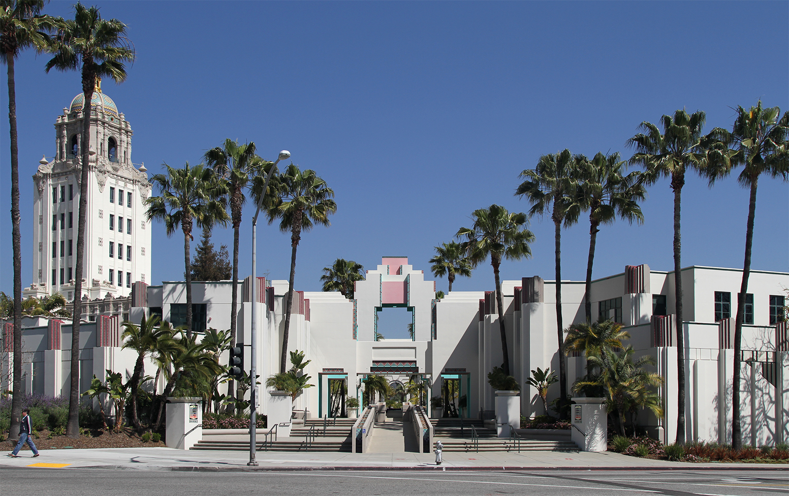 White Art Deco civic center building with a tall city hall tower and palm trees.