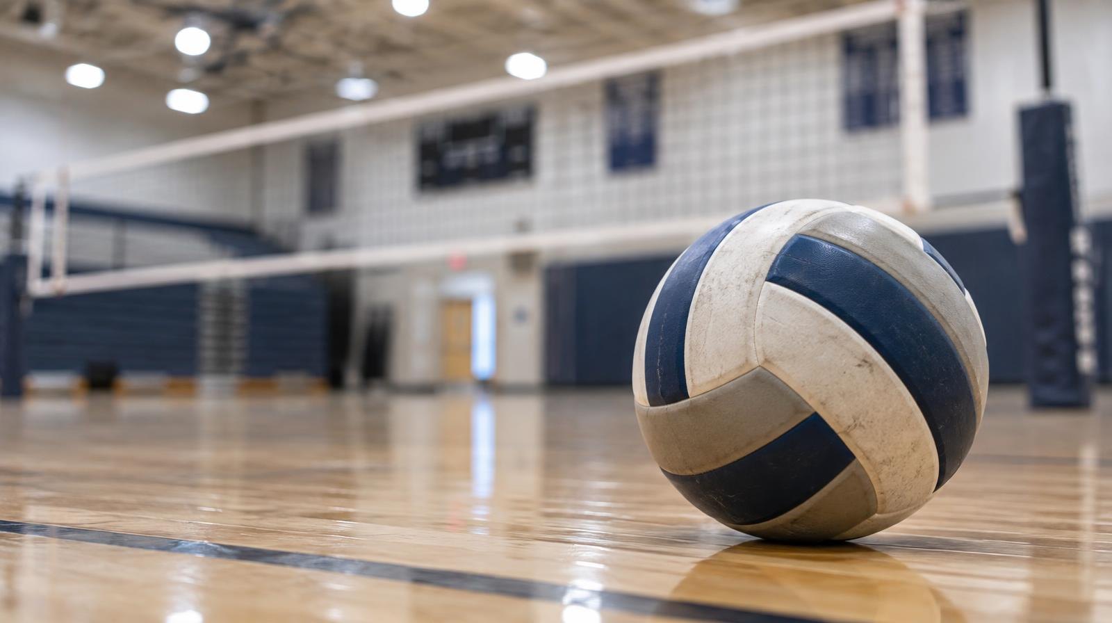 A volleyball resting on a hardwood gym floor near the net.