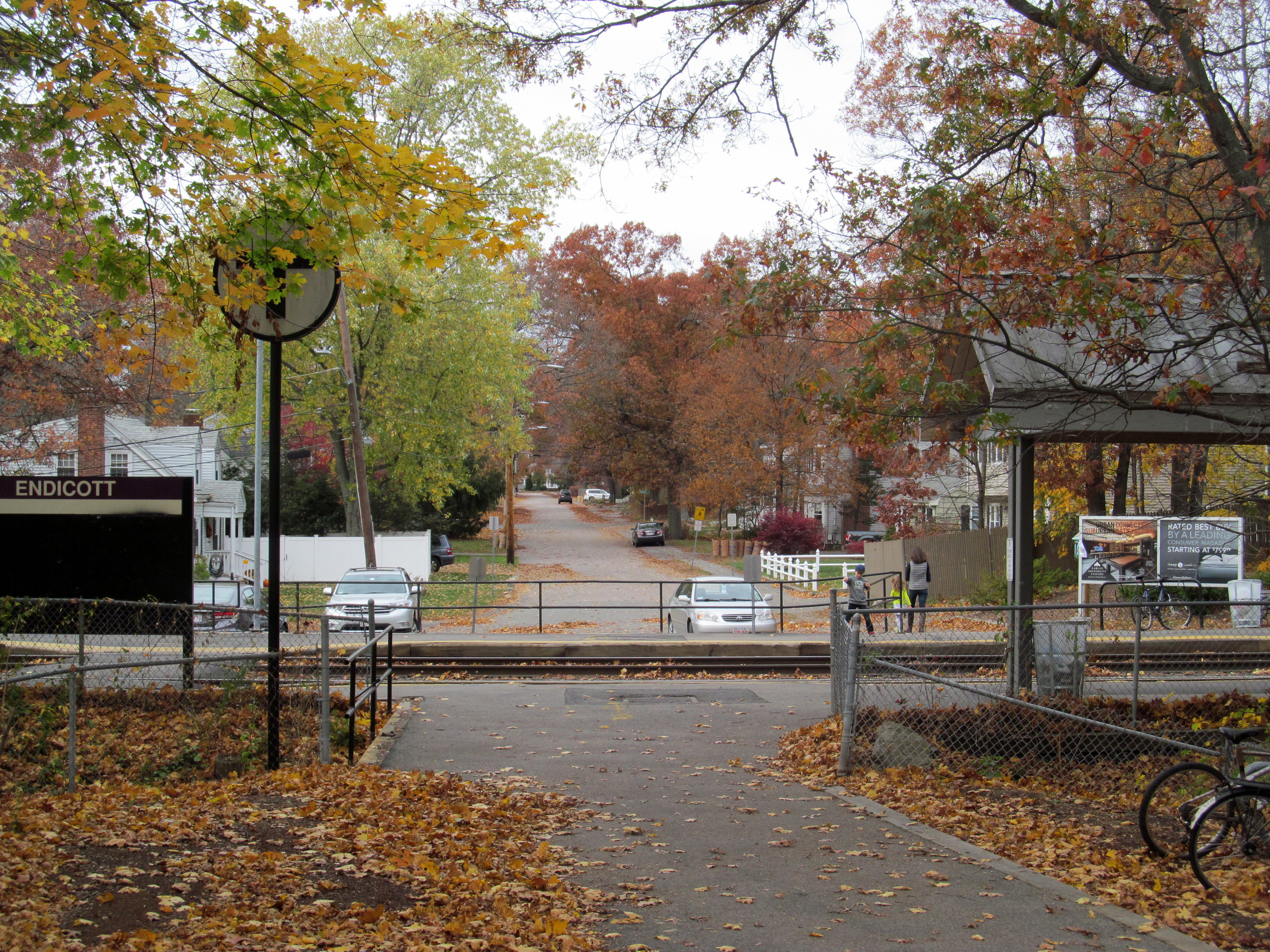 Pedestrian path leading to a commuter rail station entrance lined with autumn trees.