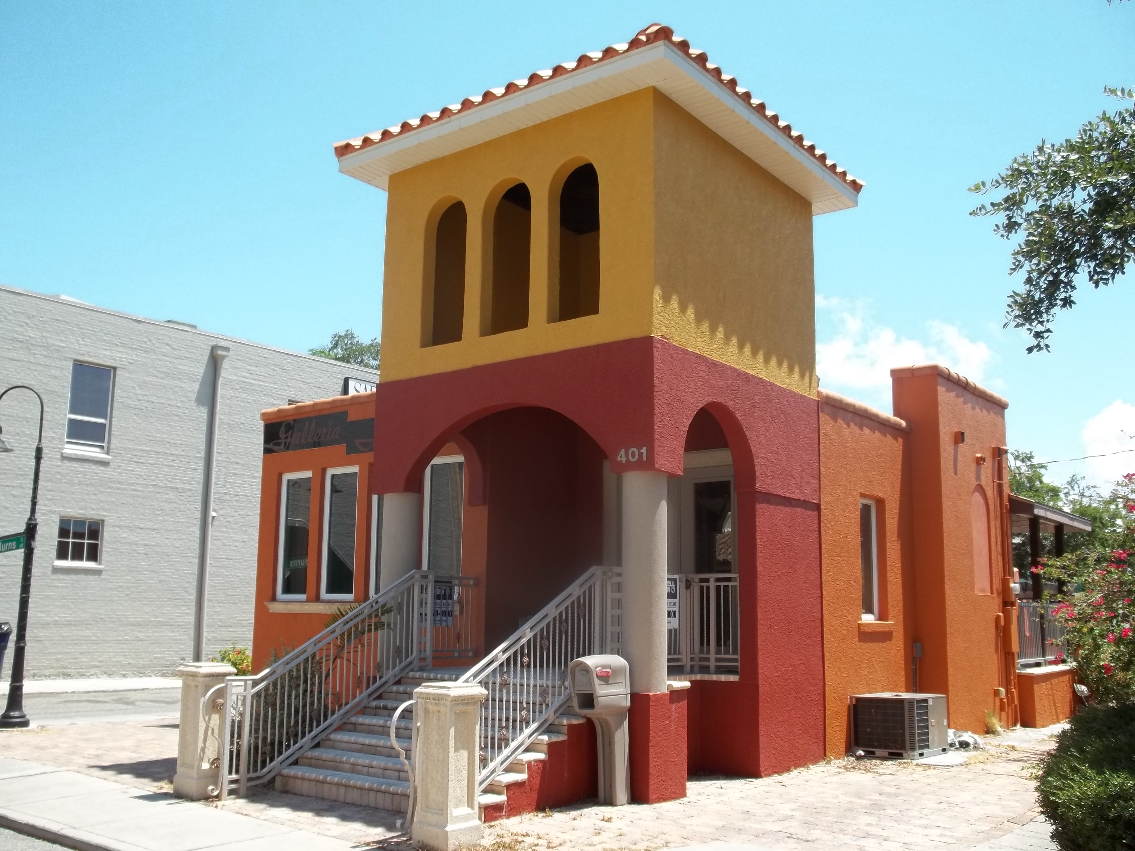 Two-story Mediterranean Revival stucco building with arched entryway and tiled tower.