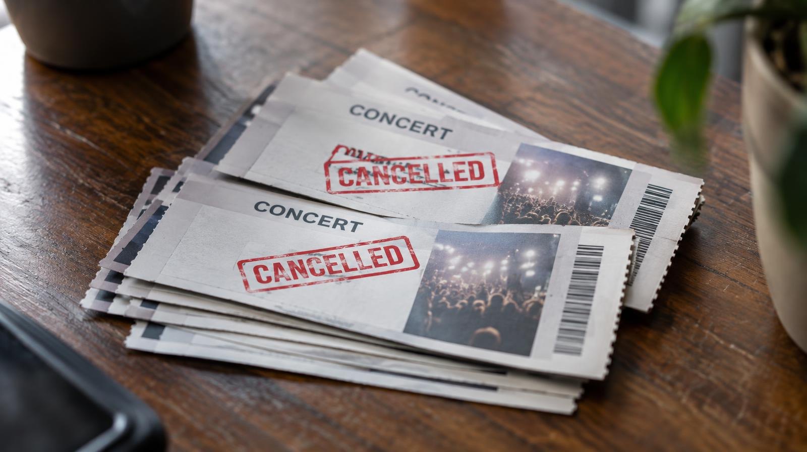 Fanned-out printed concert tickets on a wooden surface, some stamped with a red cancellation mark.