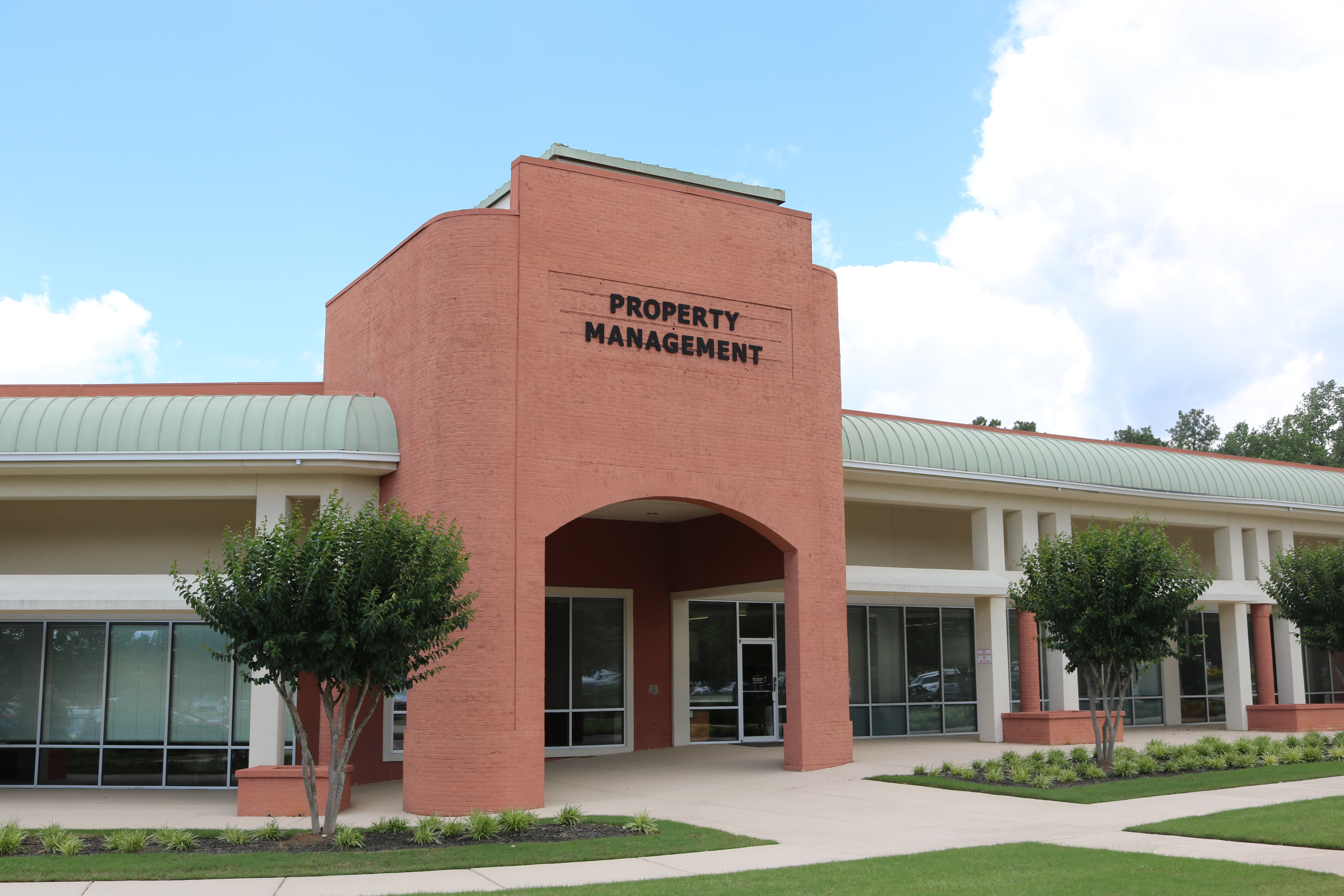 Red brick government building with a green metal roof canopy and an arched entrance labeled Property Management.