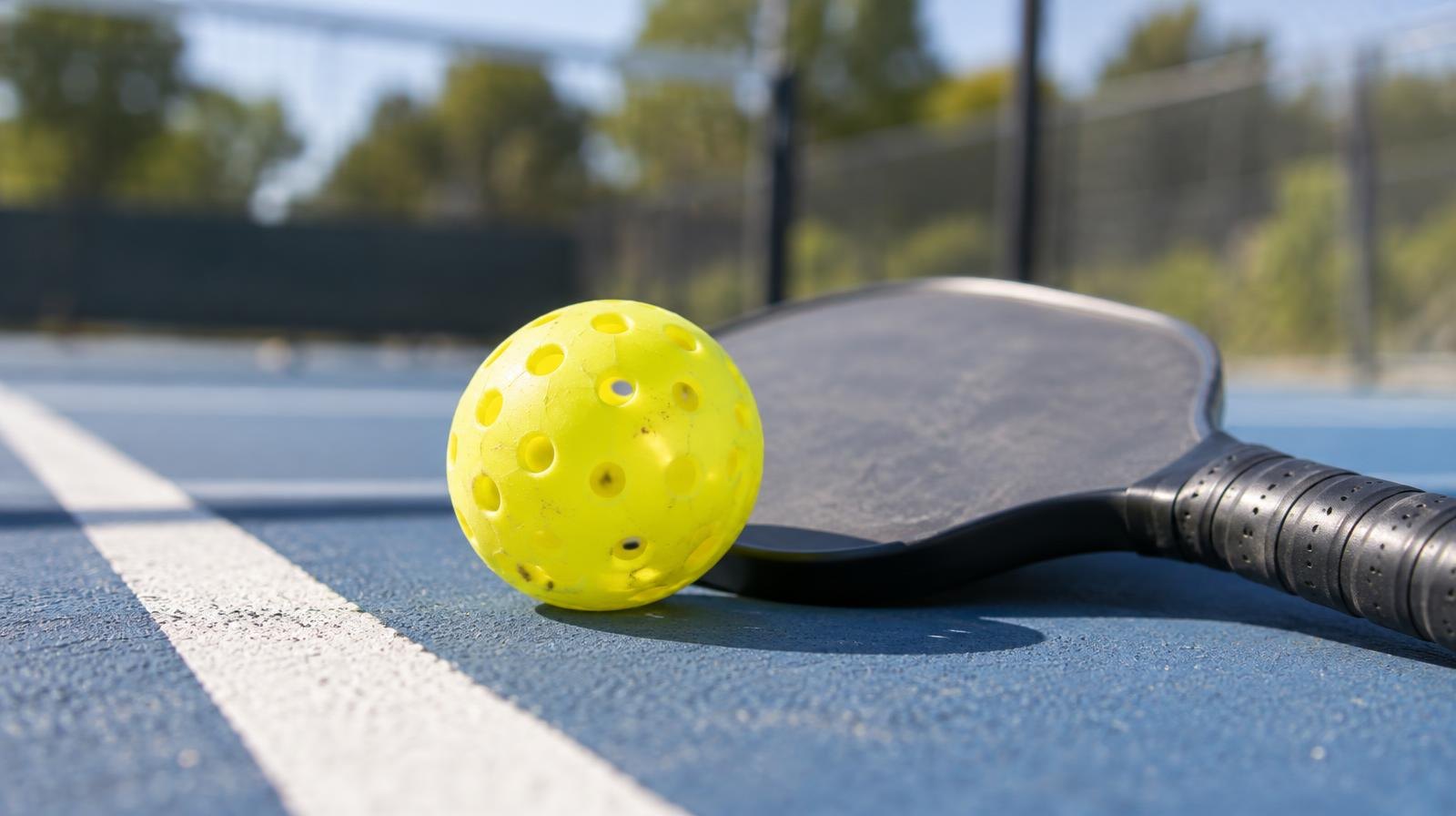 Yellow pickleball and paddle on a blue outdoor hard court.