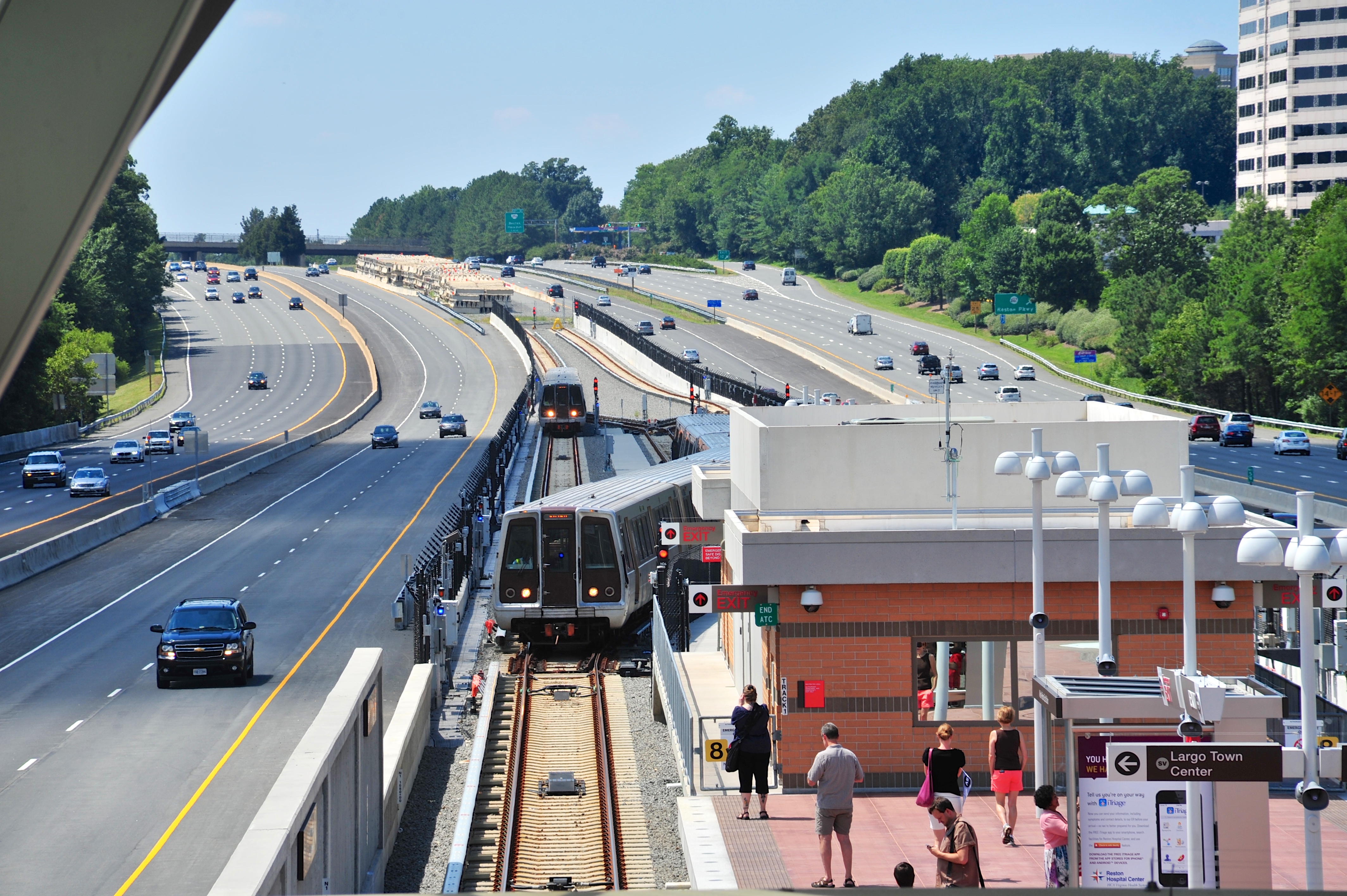 Elevated view of a Metro station with two trains at the platform and a highway alongside.