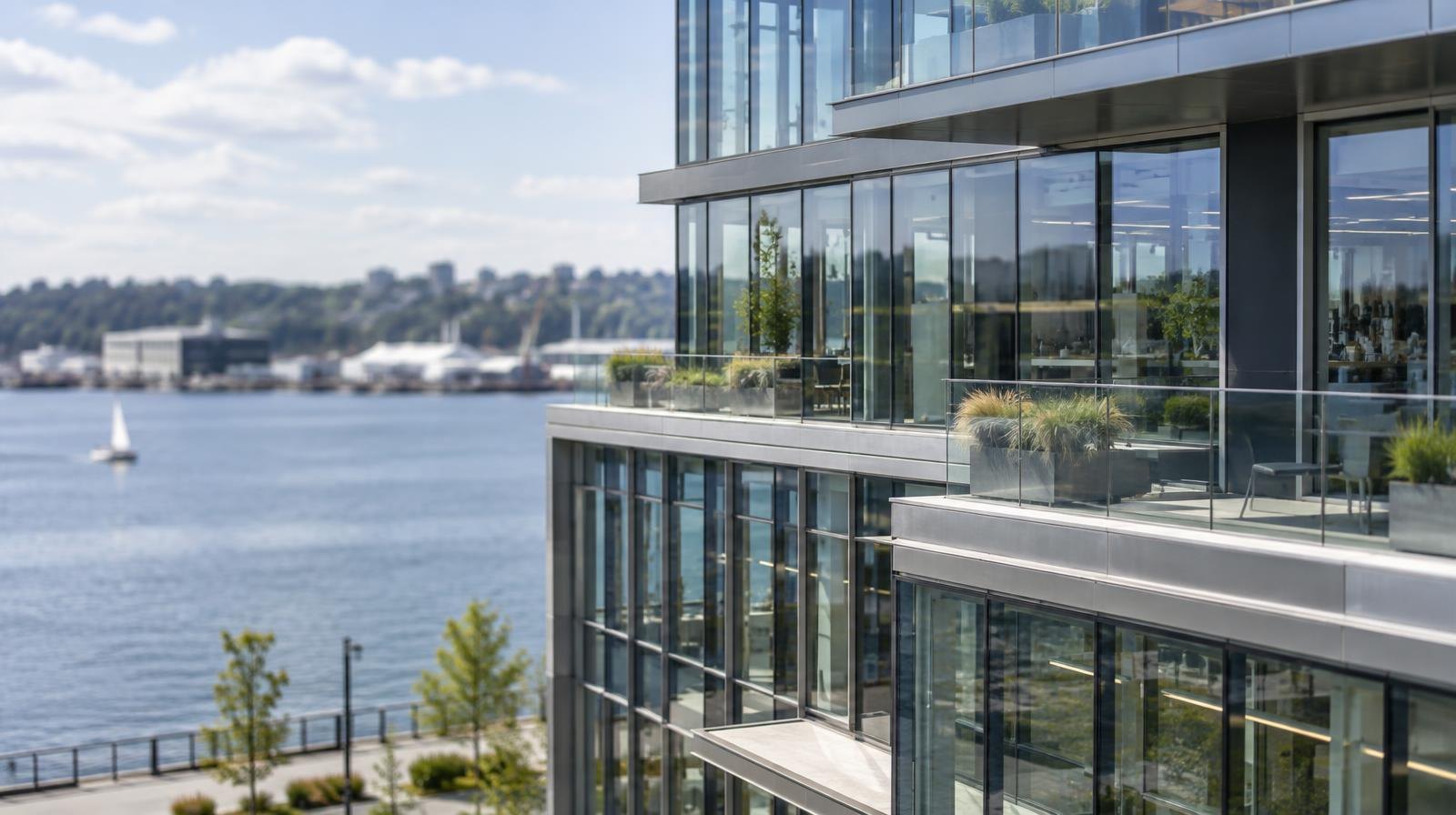 Multi-story glass office building with terraces beside calm water.