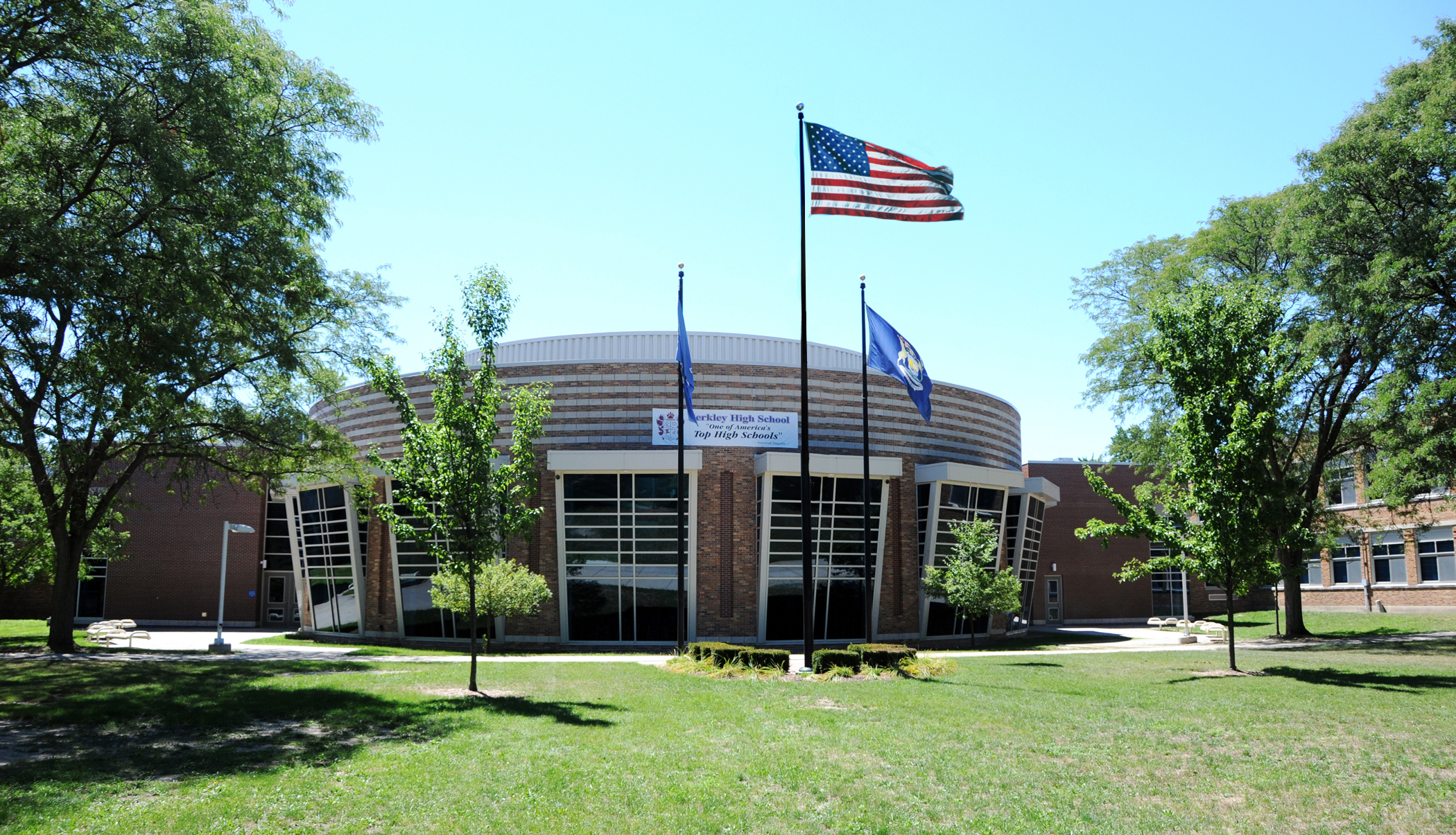 Curved brick exterior of Berkley High School with flags and trees in front.