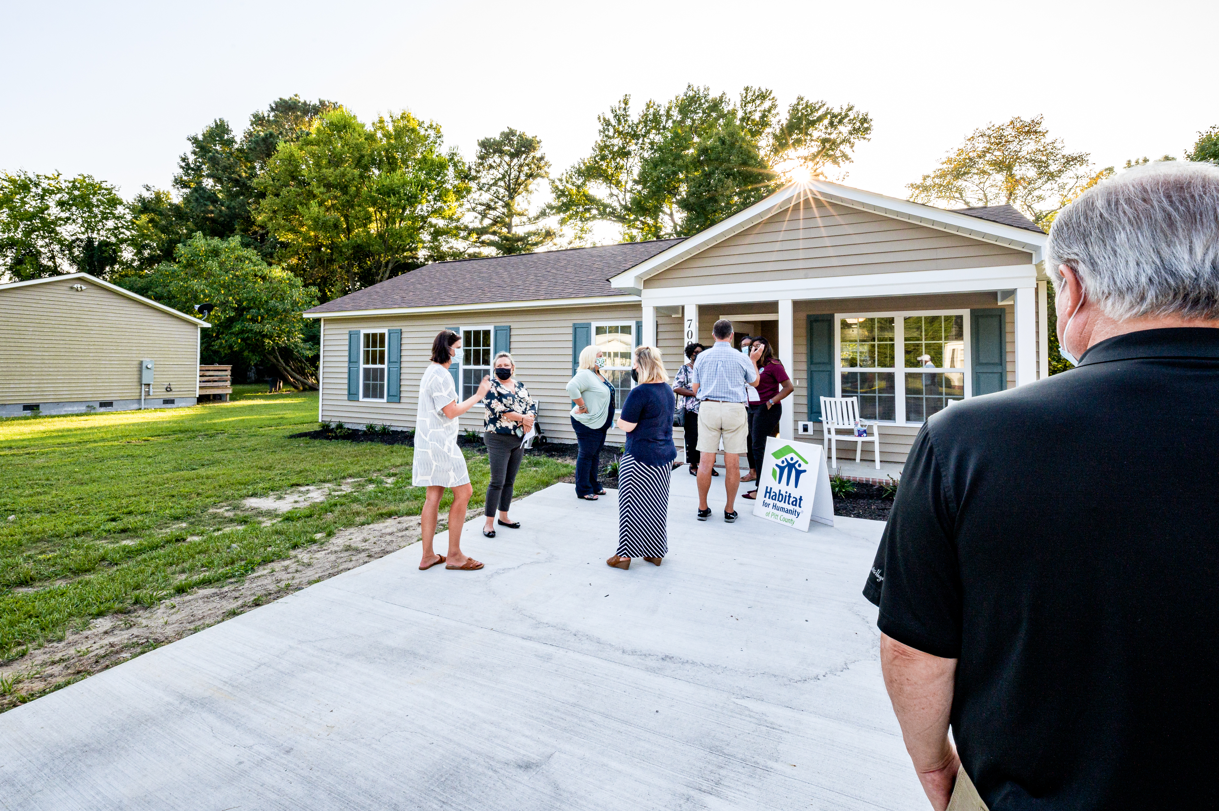 Group of people gathered on a lawn in front of a newly built home with a Habitat for Humanity sign.