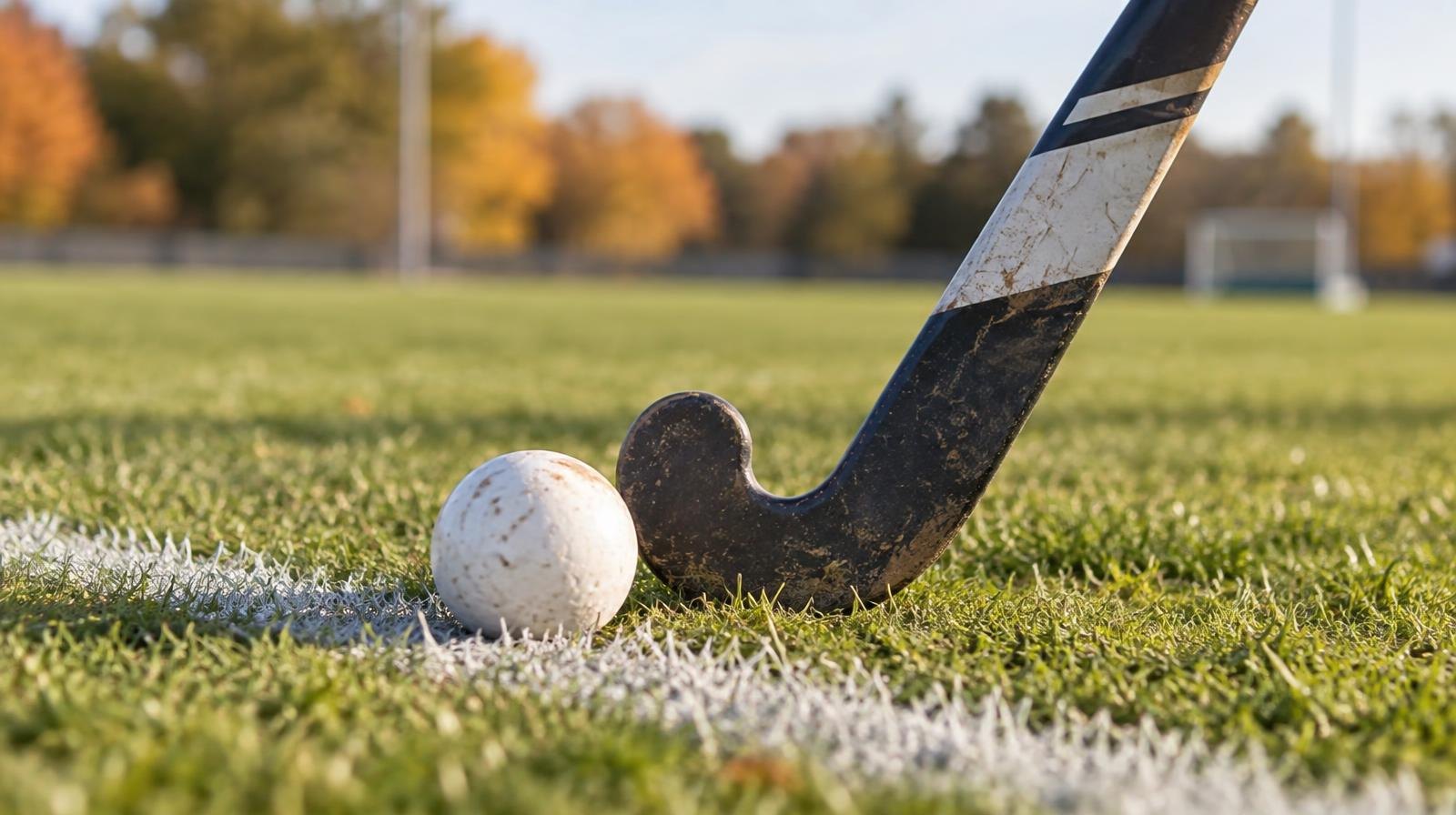 A field hockey stick and ball resting on green grass beside a white painted line.