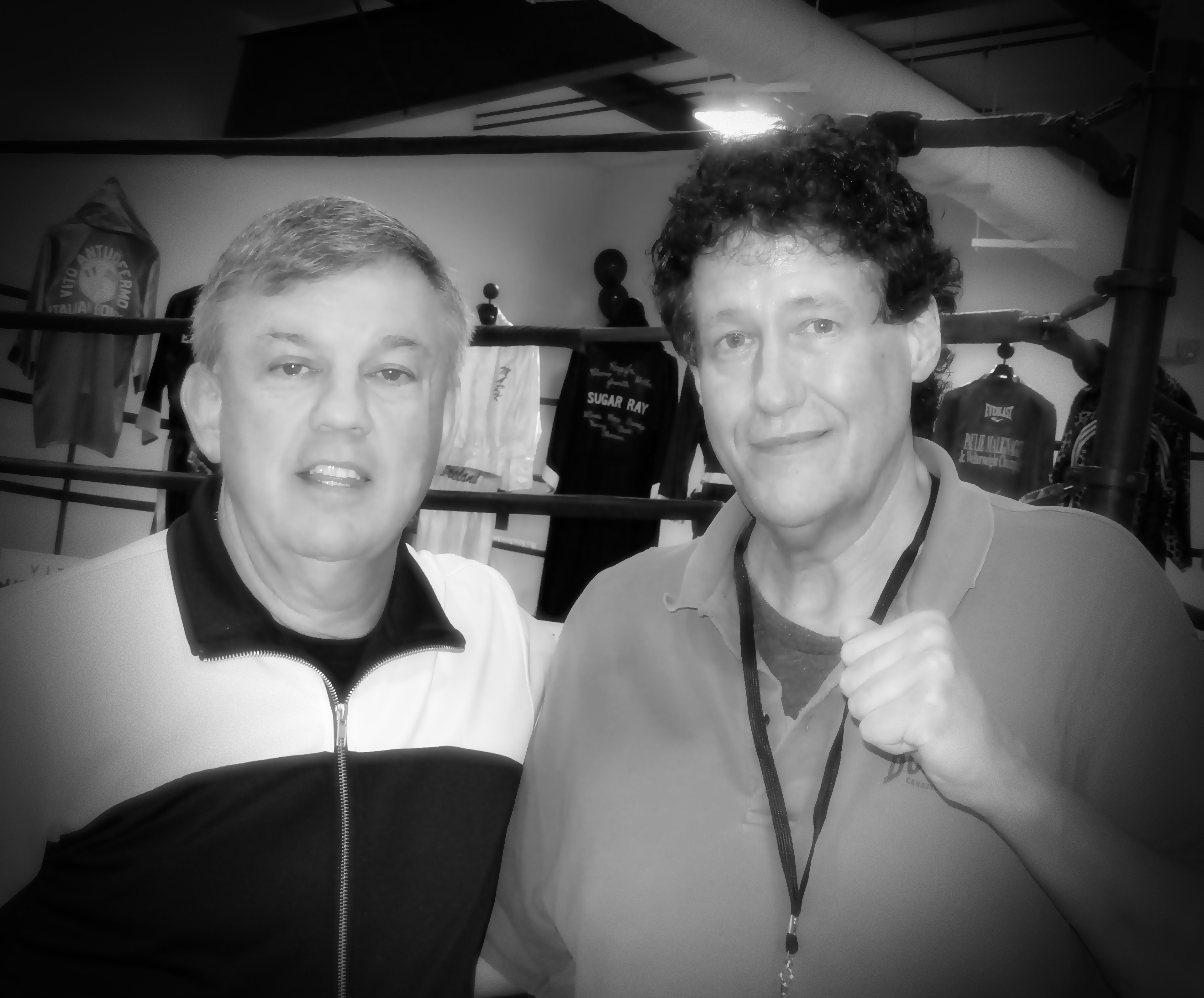 Two men pose together indoors surrounded by boxing memorabilia and signage.